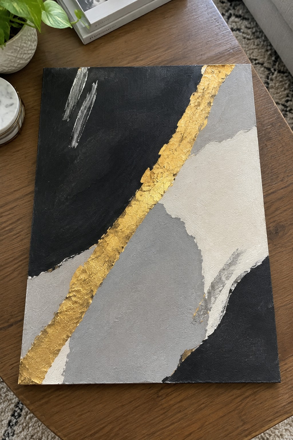 Abstract painting with black, gray sections and gold leaf on wooden table