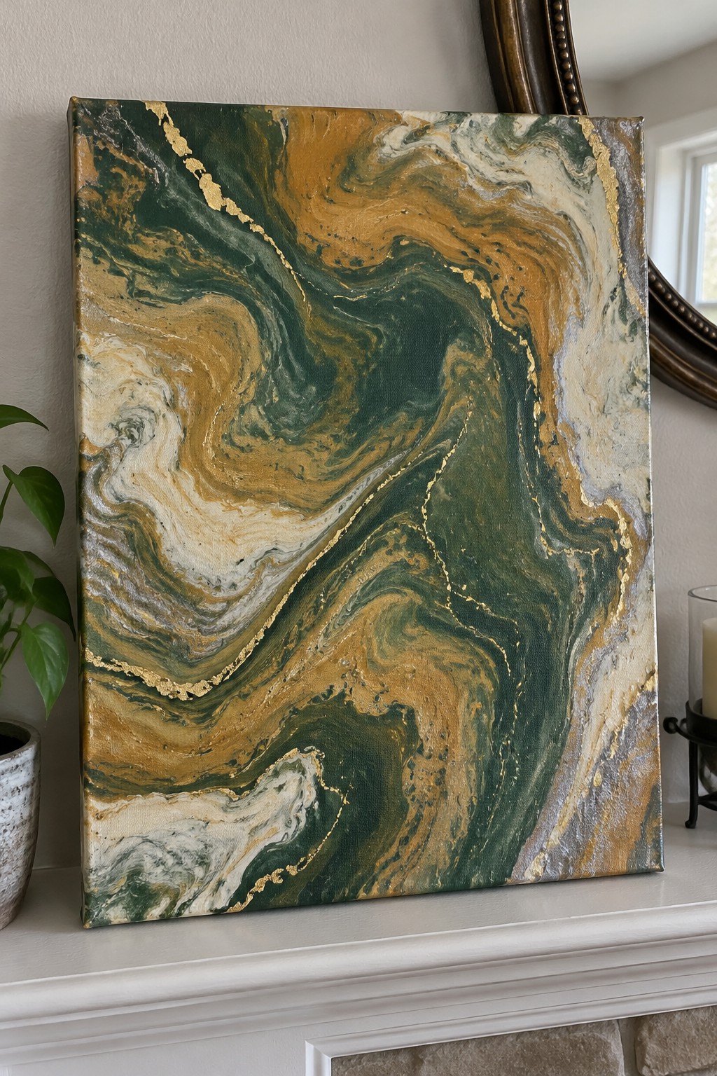 Abstract fluid painting with green, gold, and brown swirls on white mantel beside plant