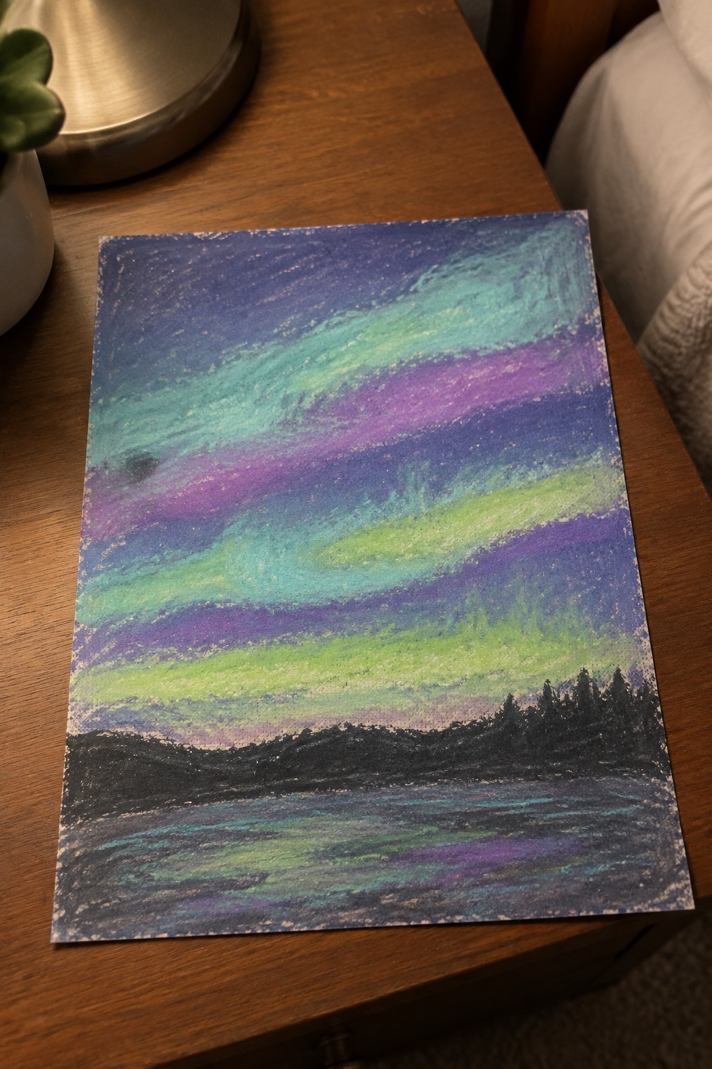 Vibrant pastel drawing of aurora borealis over mountains, trees, and water