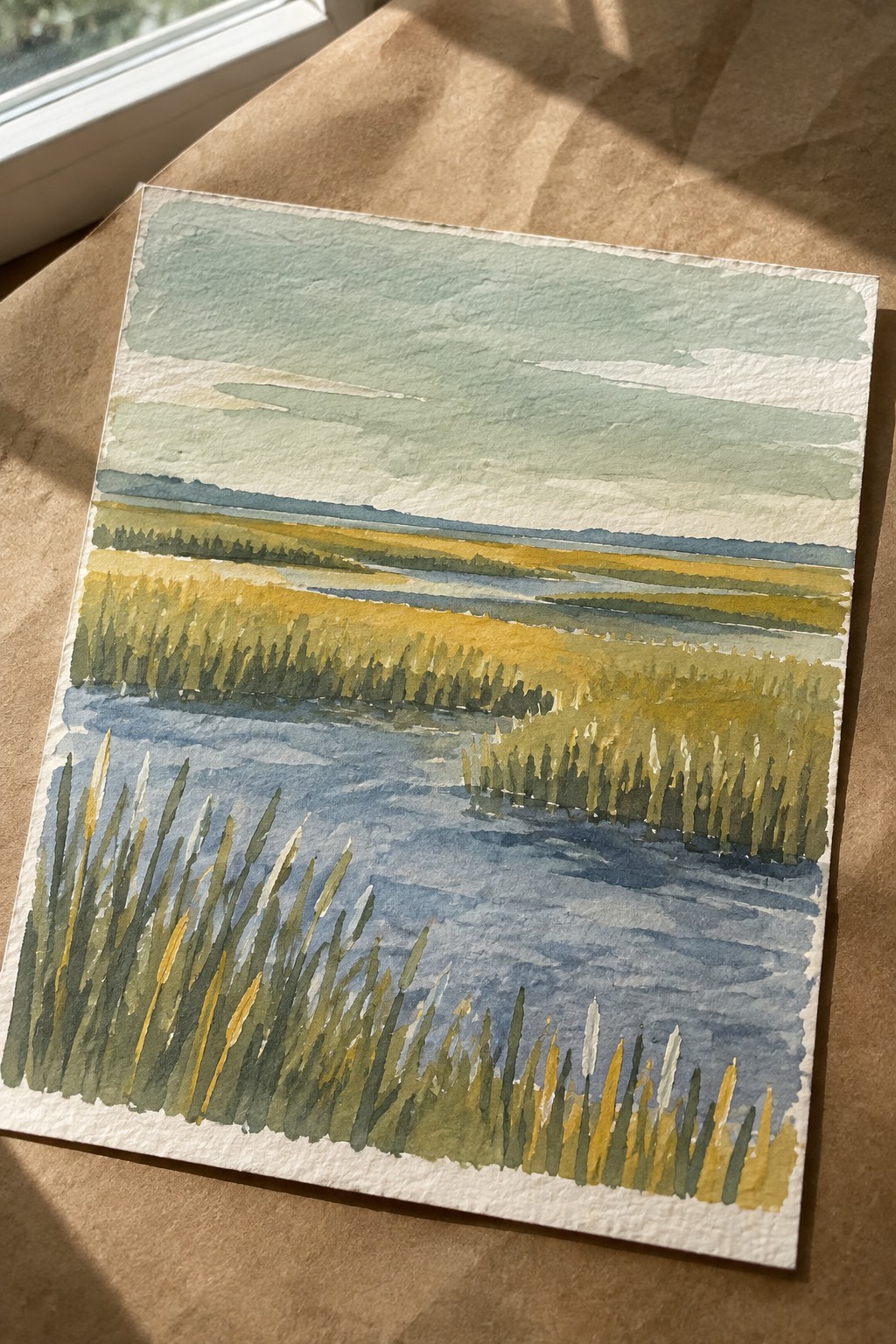 Watercolor landscape of marsh with blue water, golden reeds, green fields, and distant hills.
