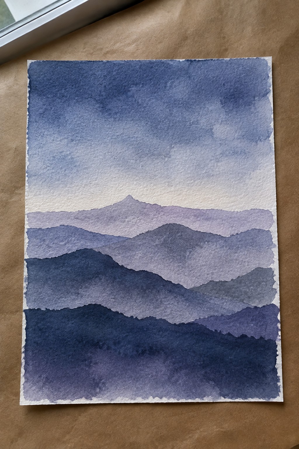 Watercolor painting of layered blue-purple mountains beneath a soft gradient sky