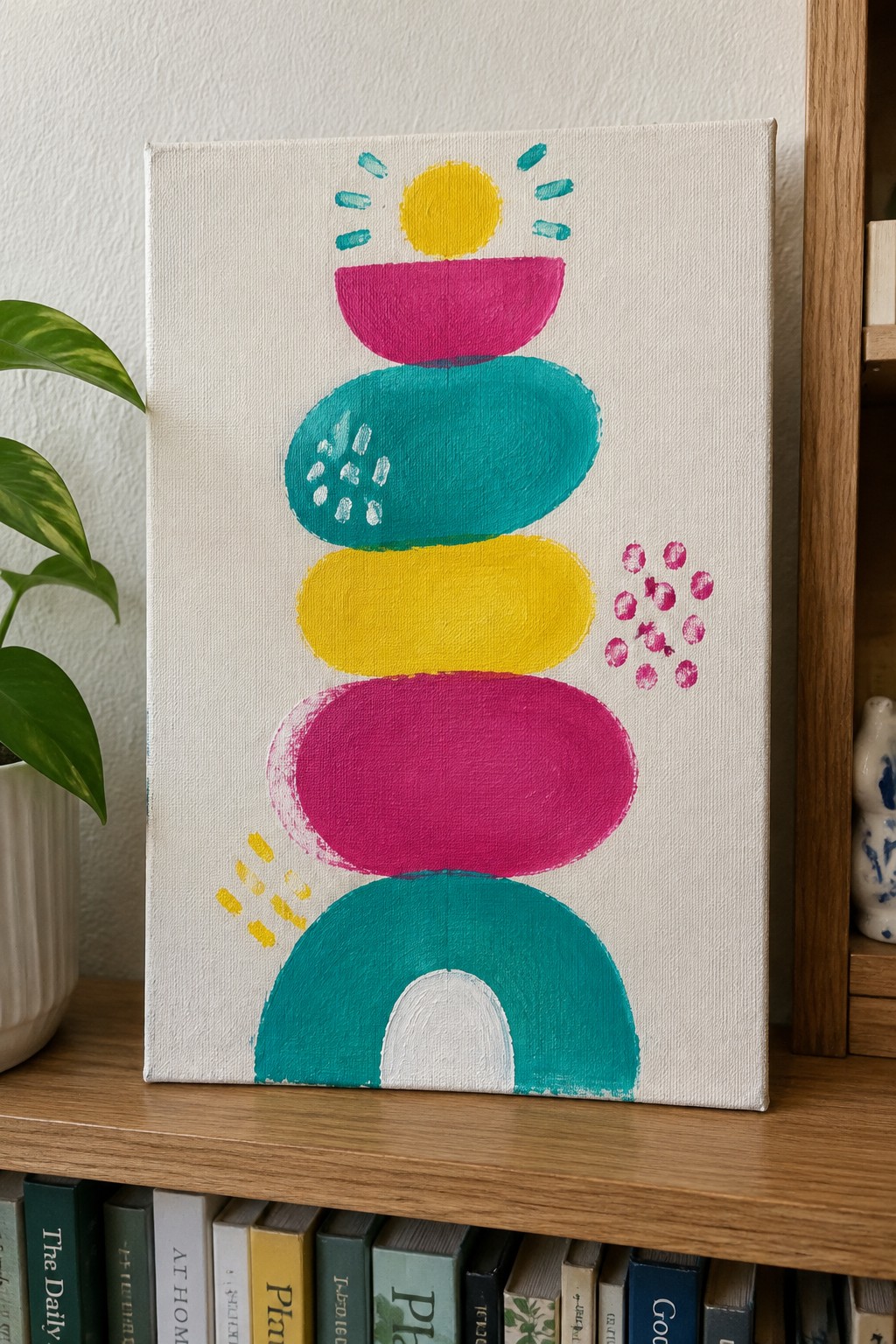 Colorful abstract painting of stacked shapes with sun on wooden bookshelf