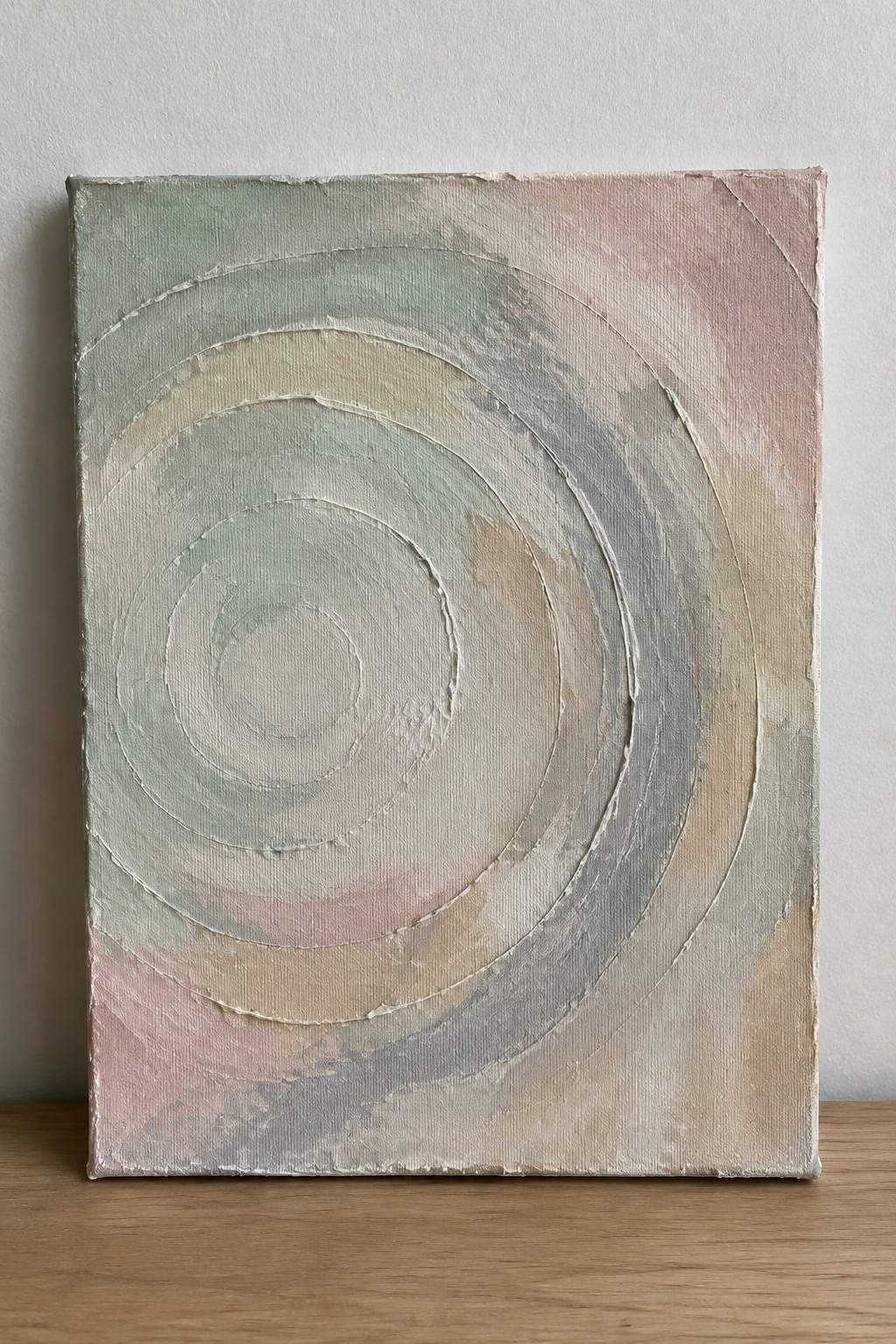 Abstract canvas with soft pastel concentric circles and swirls on wooden floor