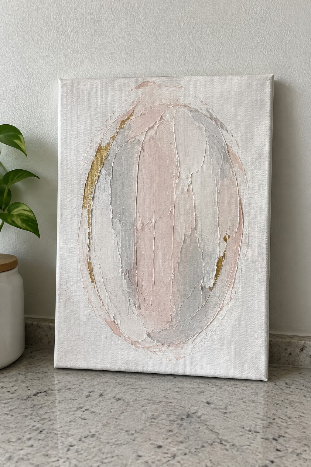 Abstract oval painting with pink, gray, and gold textures on white canvas