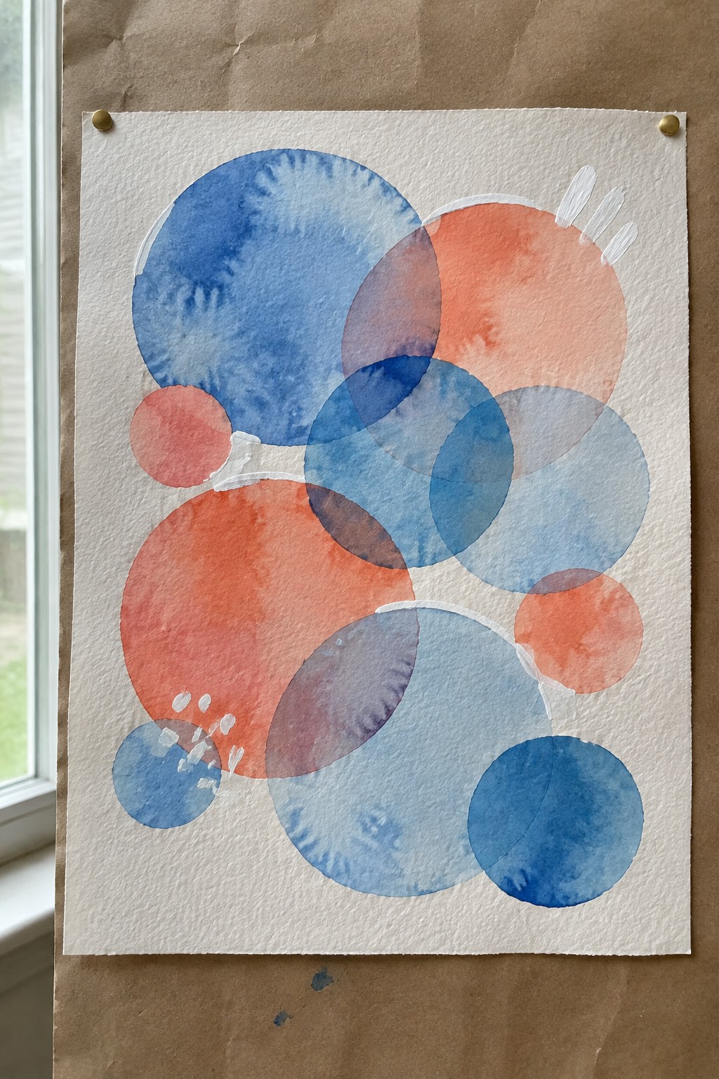 Abstract watercolor with overlapping blue, orange, and purple circles pinned to brown paper