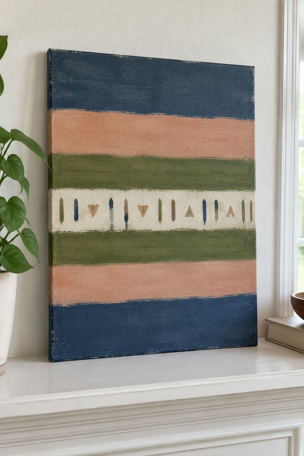 Abstract striped painting with navy, peach, and green bands on mantel beside plant and books.