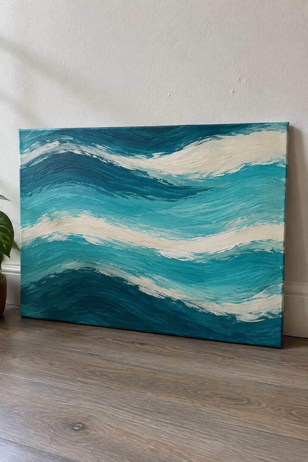 Abstract teal wave painting on canvas leaning against wall on wooden floor