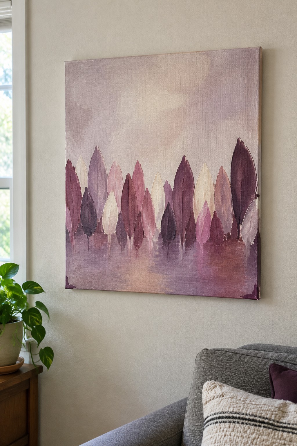 Abstract purple-pink tree painting on wall above gray couch and potted plant.