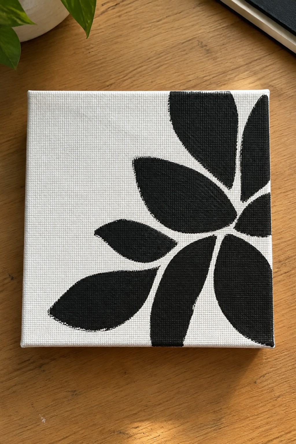 Minimalist black flower painting on white canvas atop wooden table