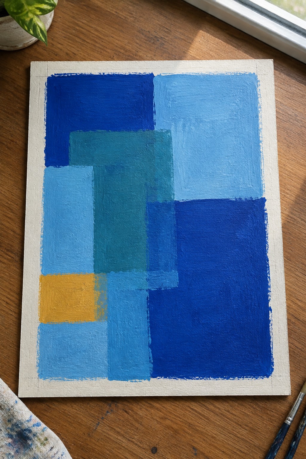 Abstract painting with overlapping blue rectangles, teal shapes, and yellow square on canvas.