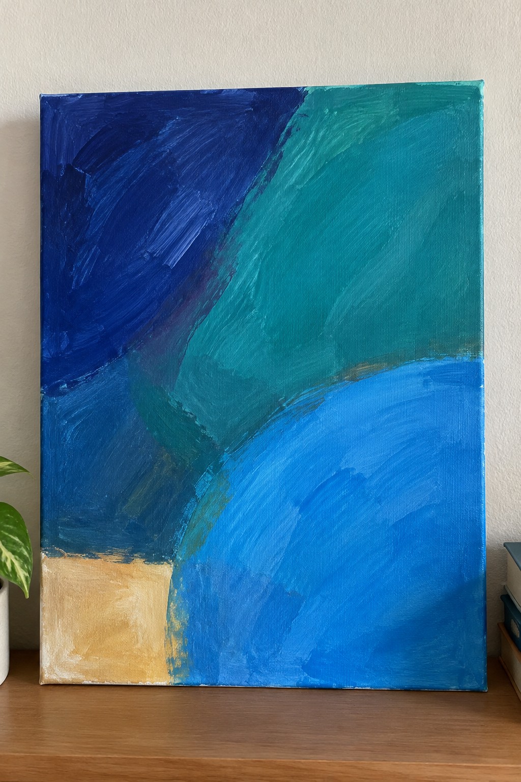 Abstract canvas with bold blue, teal, and yellow brushstrokes on wooden surface