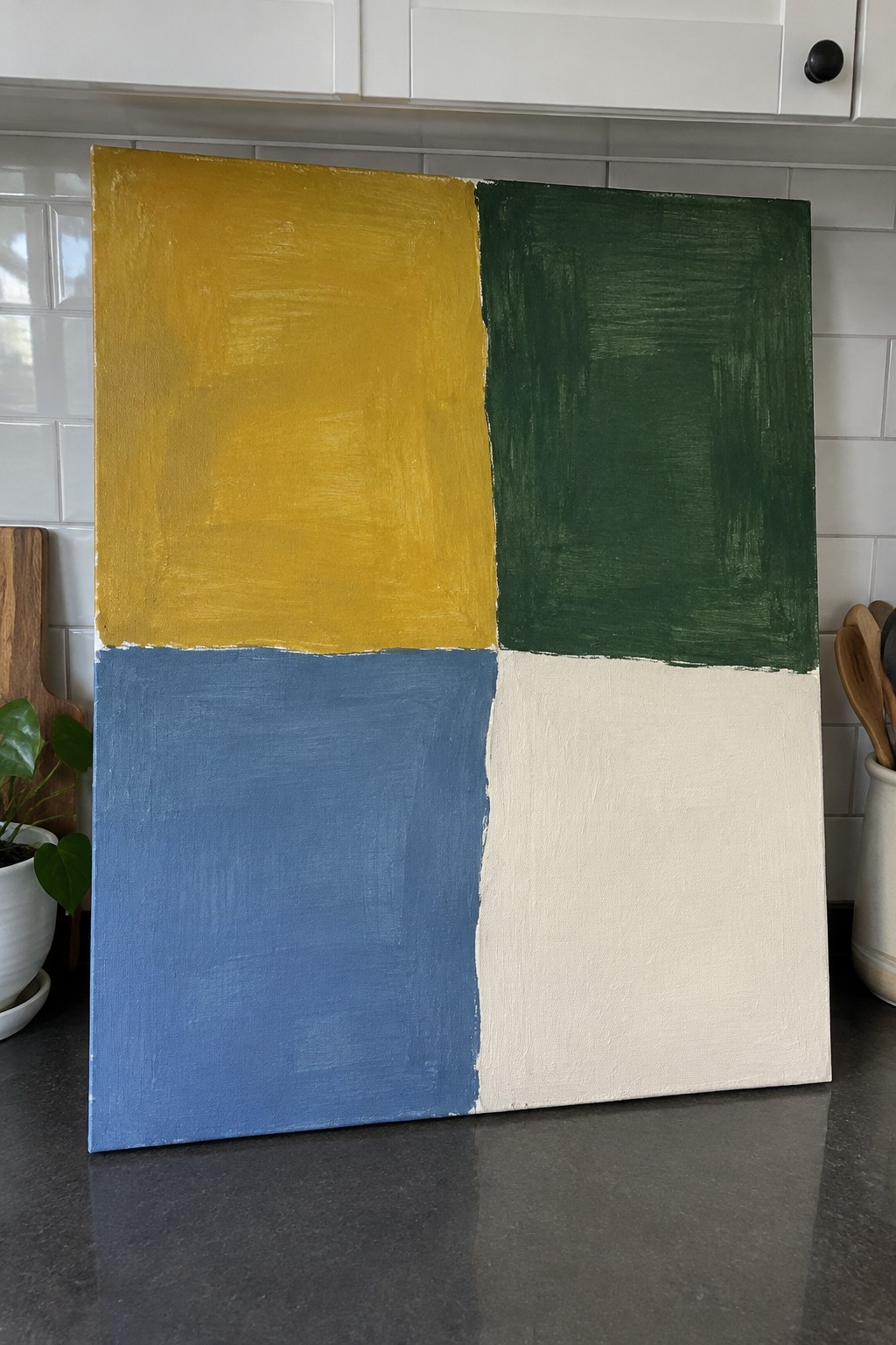 Abstract painting in four quadrants: yellow, green, blue, and cream, leaning in kitchen.