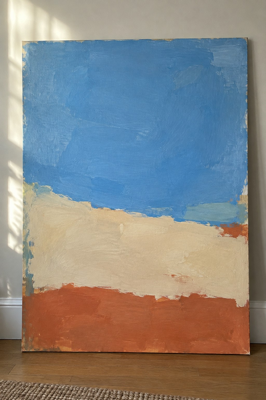 Abstract painting with blue top, cream middle, and orange bottom leaning on wall