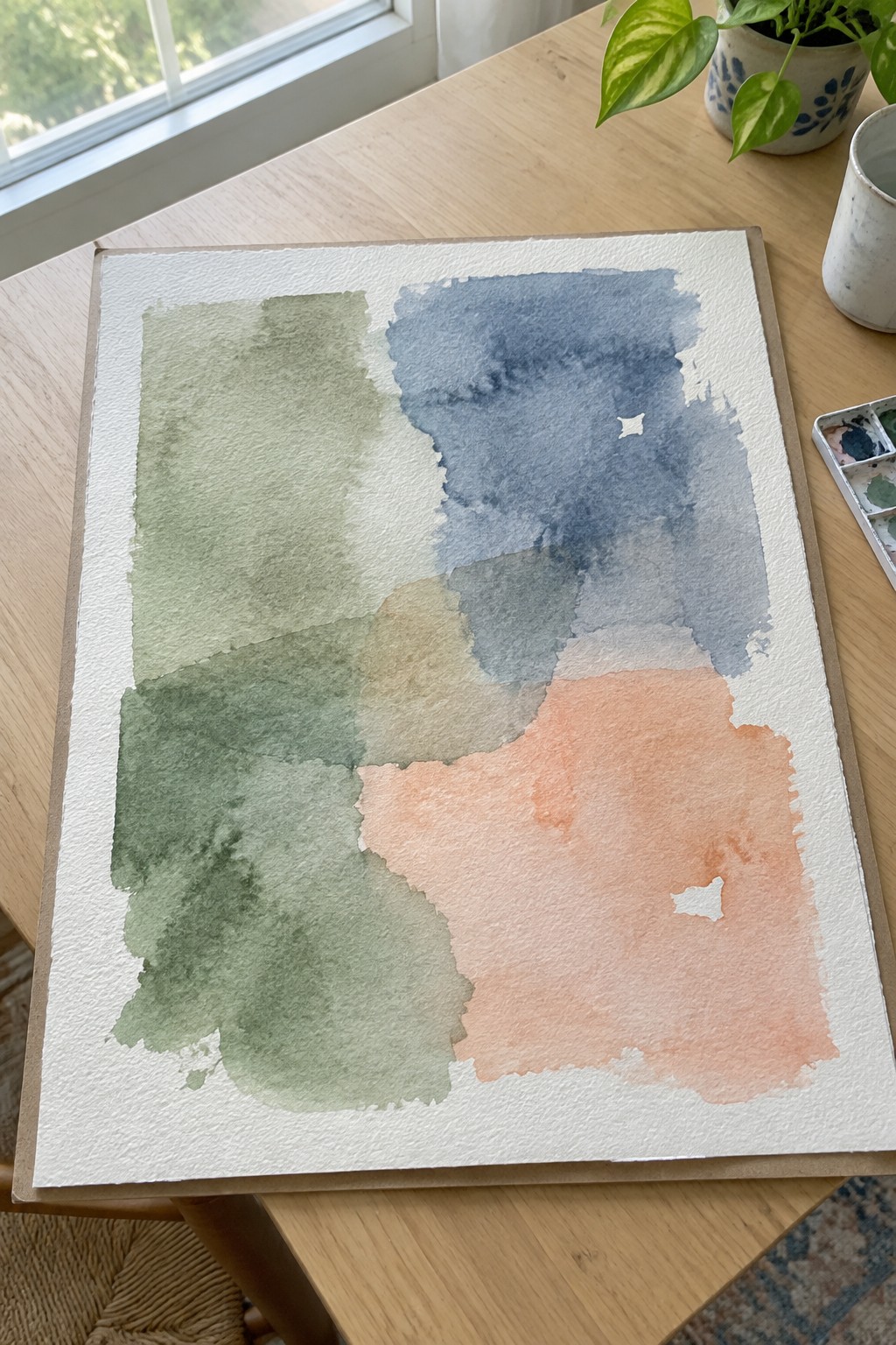 Abstract watercolor painting with green, blue, beige and peach washes on wooden table