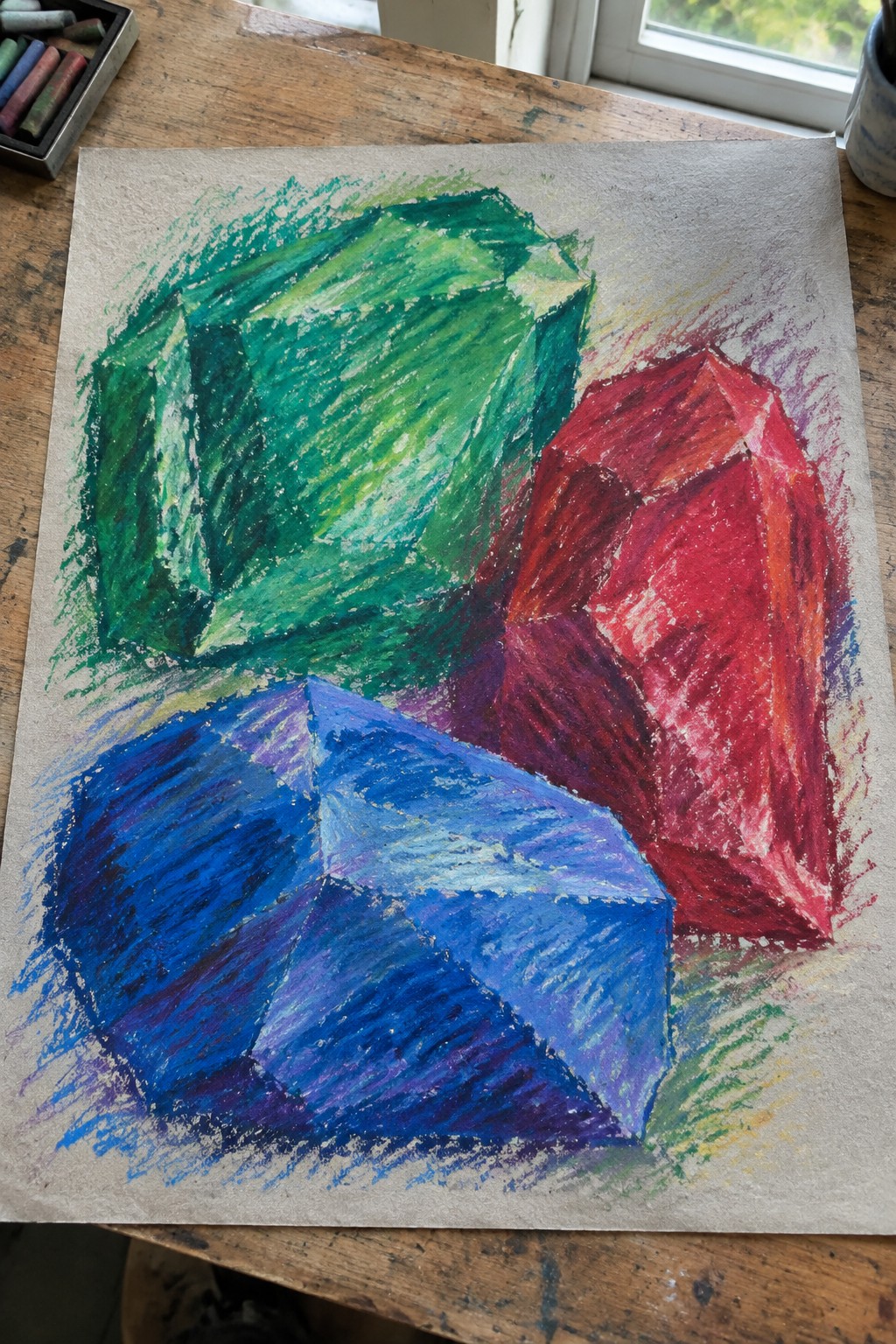 Pastel drawing of green, red, and blue faceted crystals on wooden table