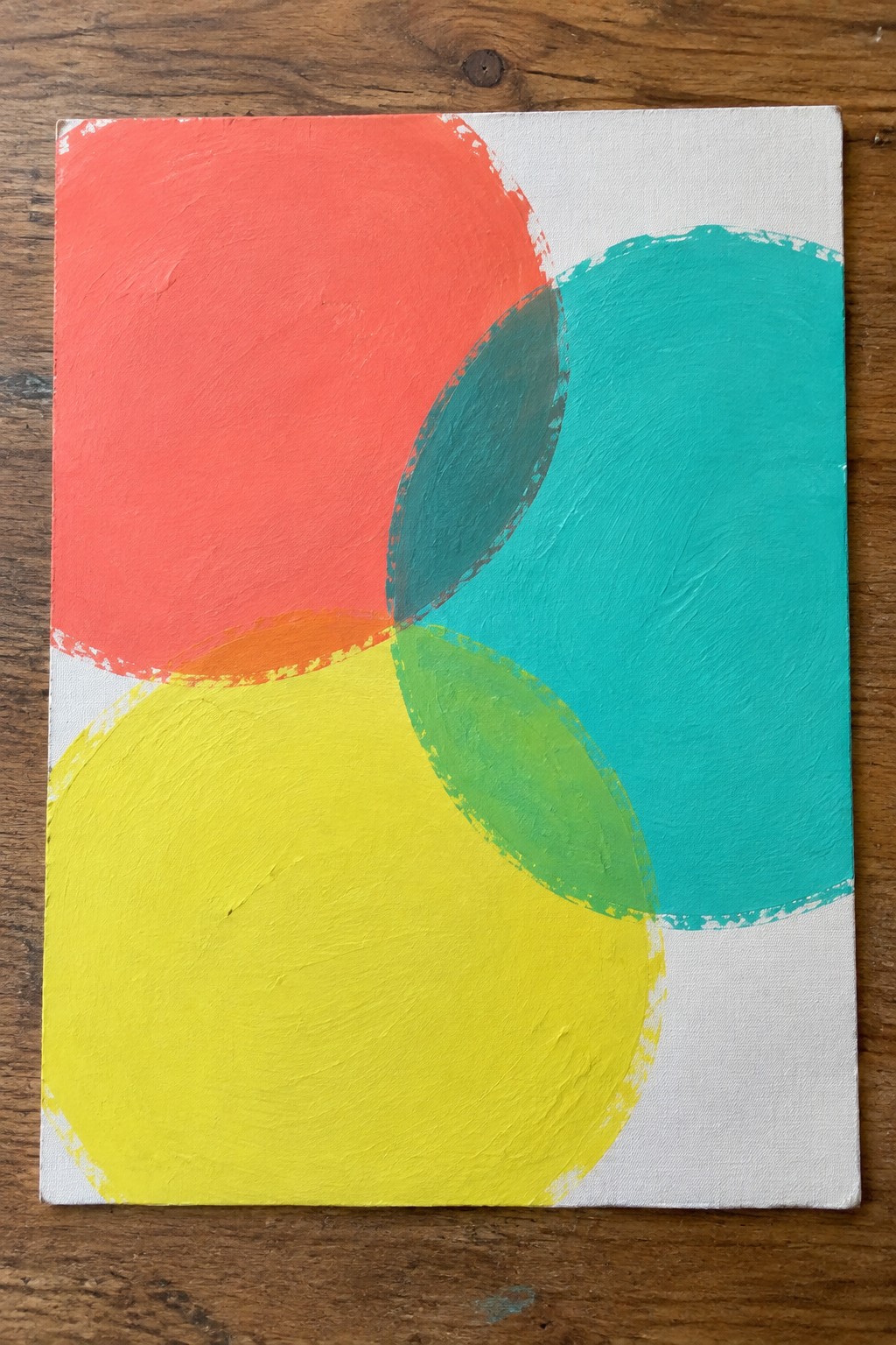 Abstract painting with overlapping red, yellow, green, and teal circles on canvas over wood.