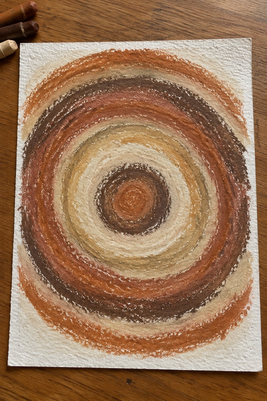 Concentric circles in earthy browns and oranges on textured white paper with crayons