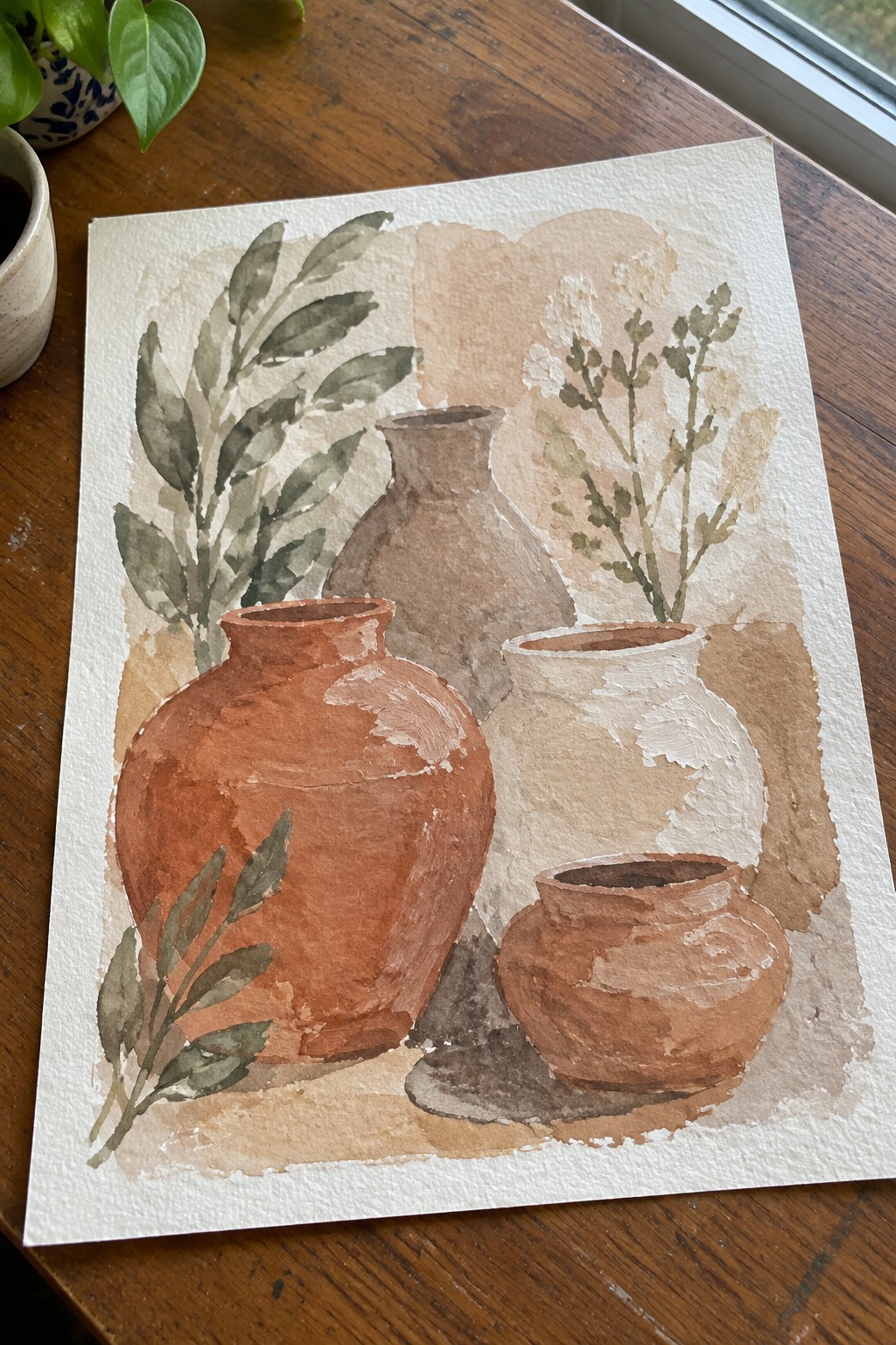 Watercolor still life of terracotta vases, white pot, and green foliage on wood