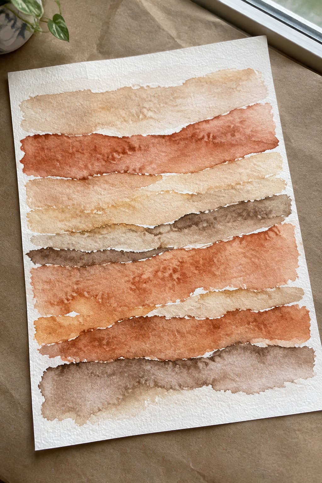 Horizontal watercolor stripes in beige, orange, terracotta and brown on white paper.