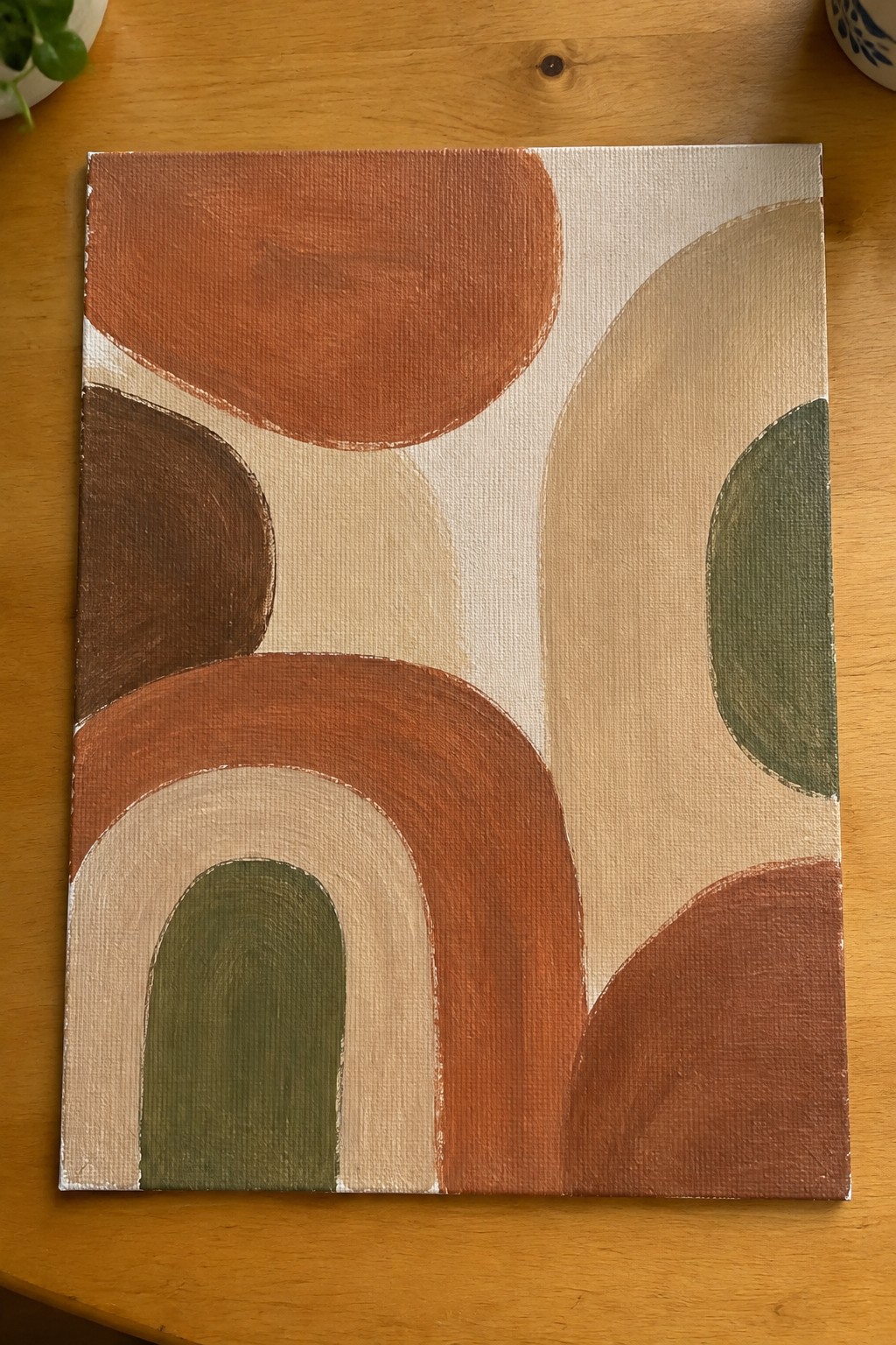 Abstract painting with earthy arches and circles in terracotta, brown, and green on wood table