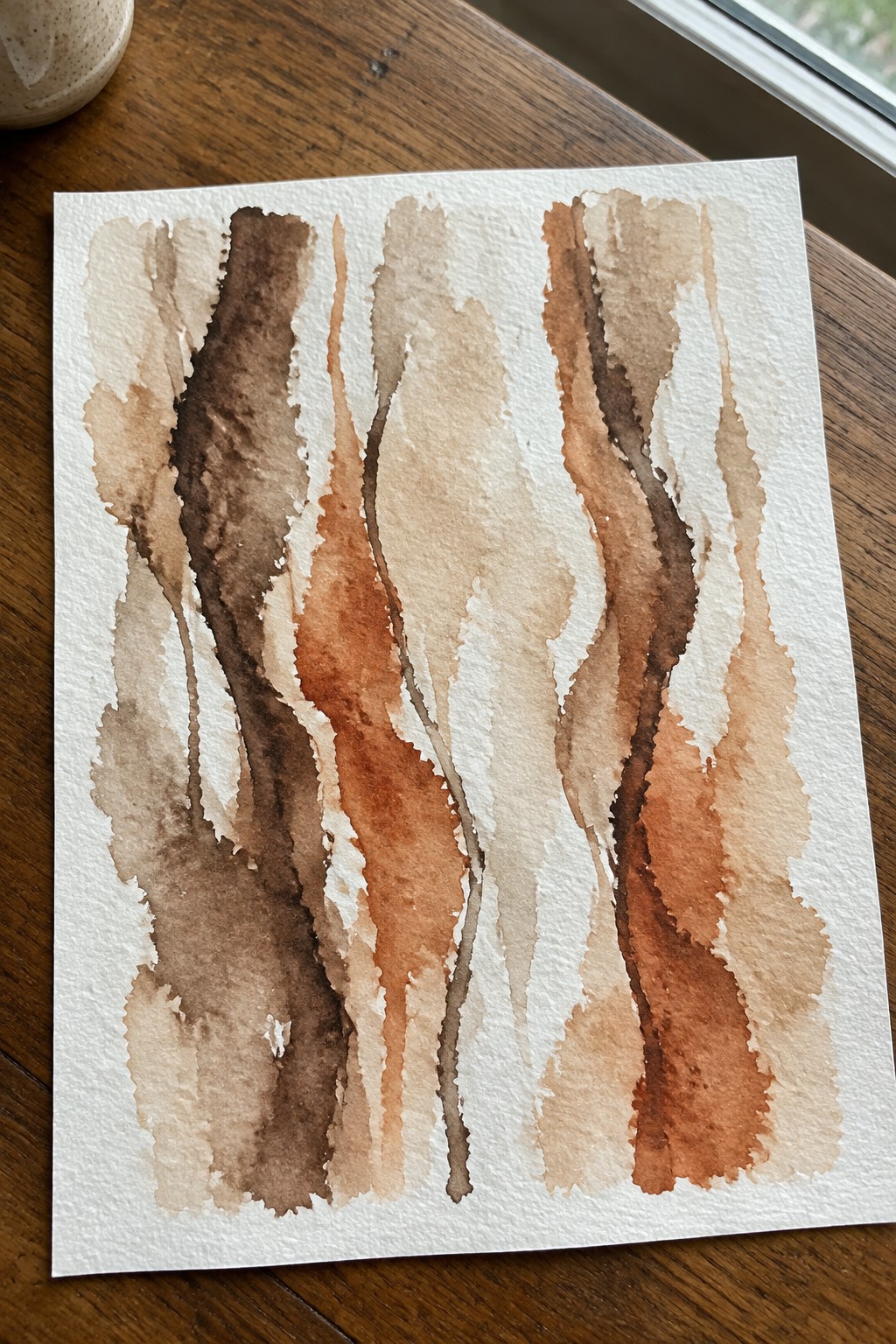 Abstract watercolor painting with vertical flowing stripes in brown earth tones on white paper