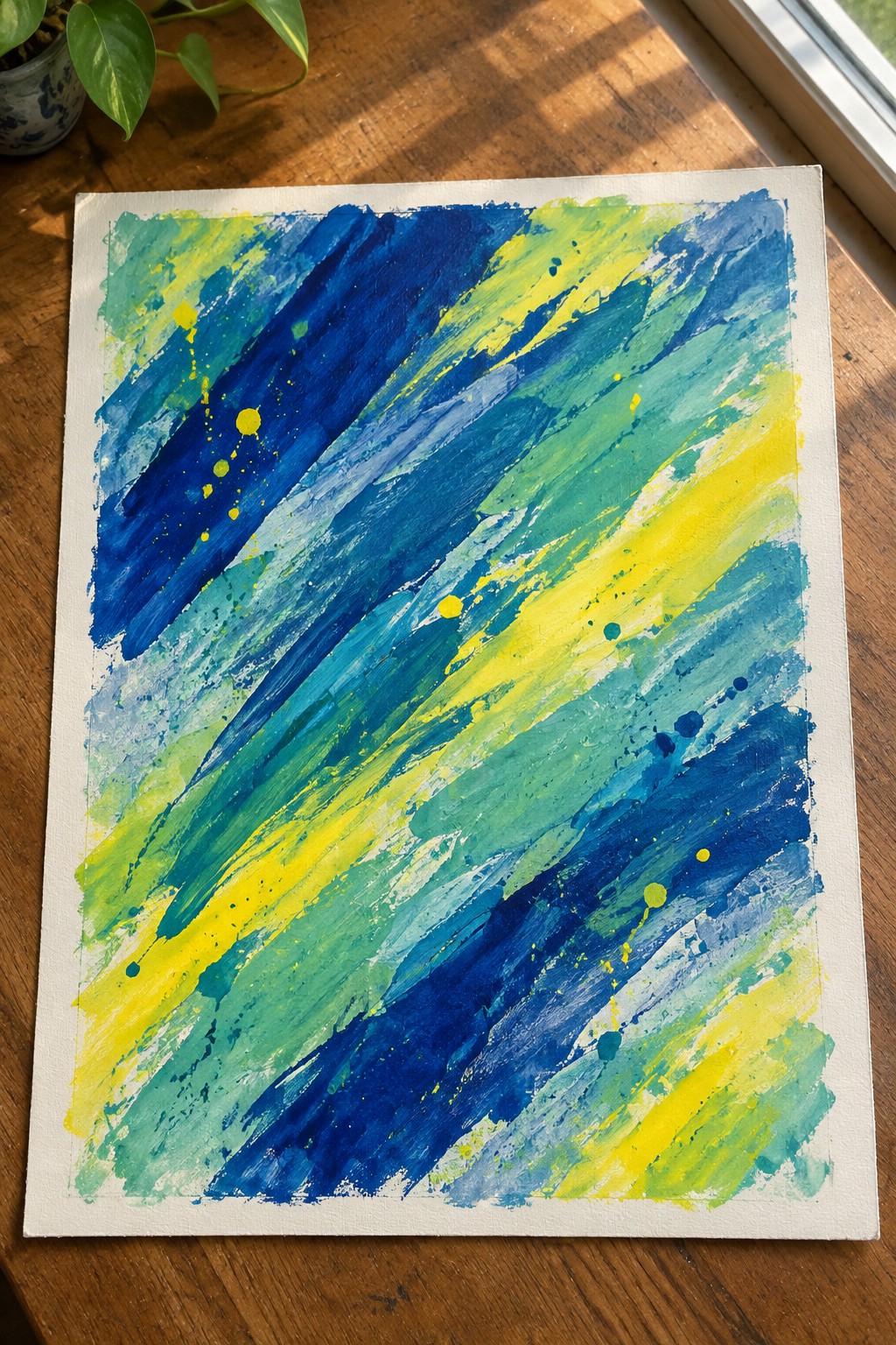 Abstract painting with bold blue, green, and yellow diagonal brushstrokes and splatters on white canvas