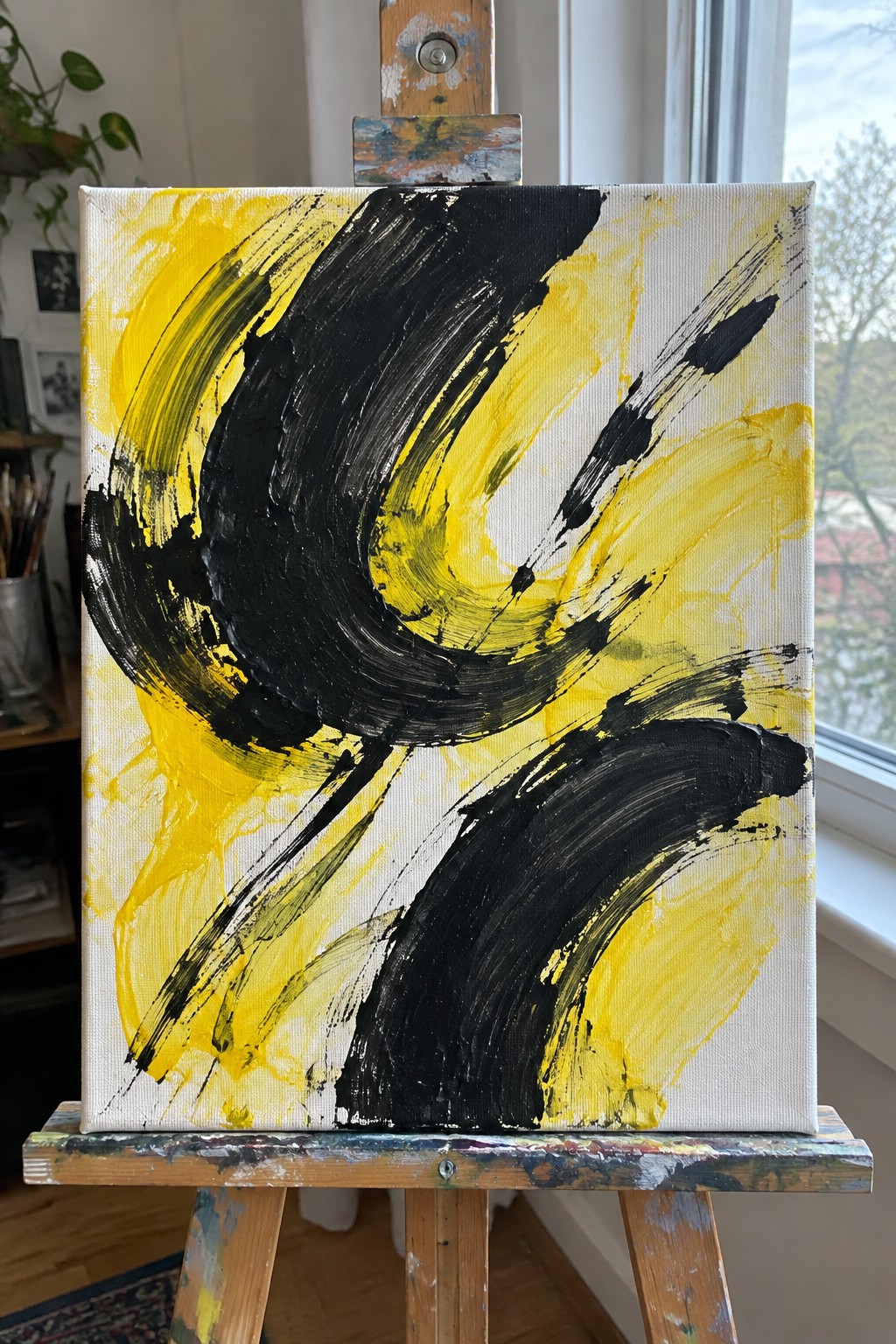 Abstract painting with bold black and yellow brushstrokes on white canvas on easel