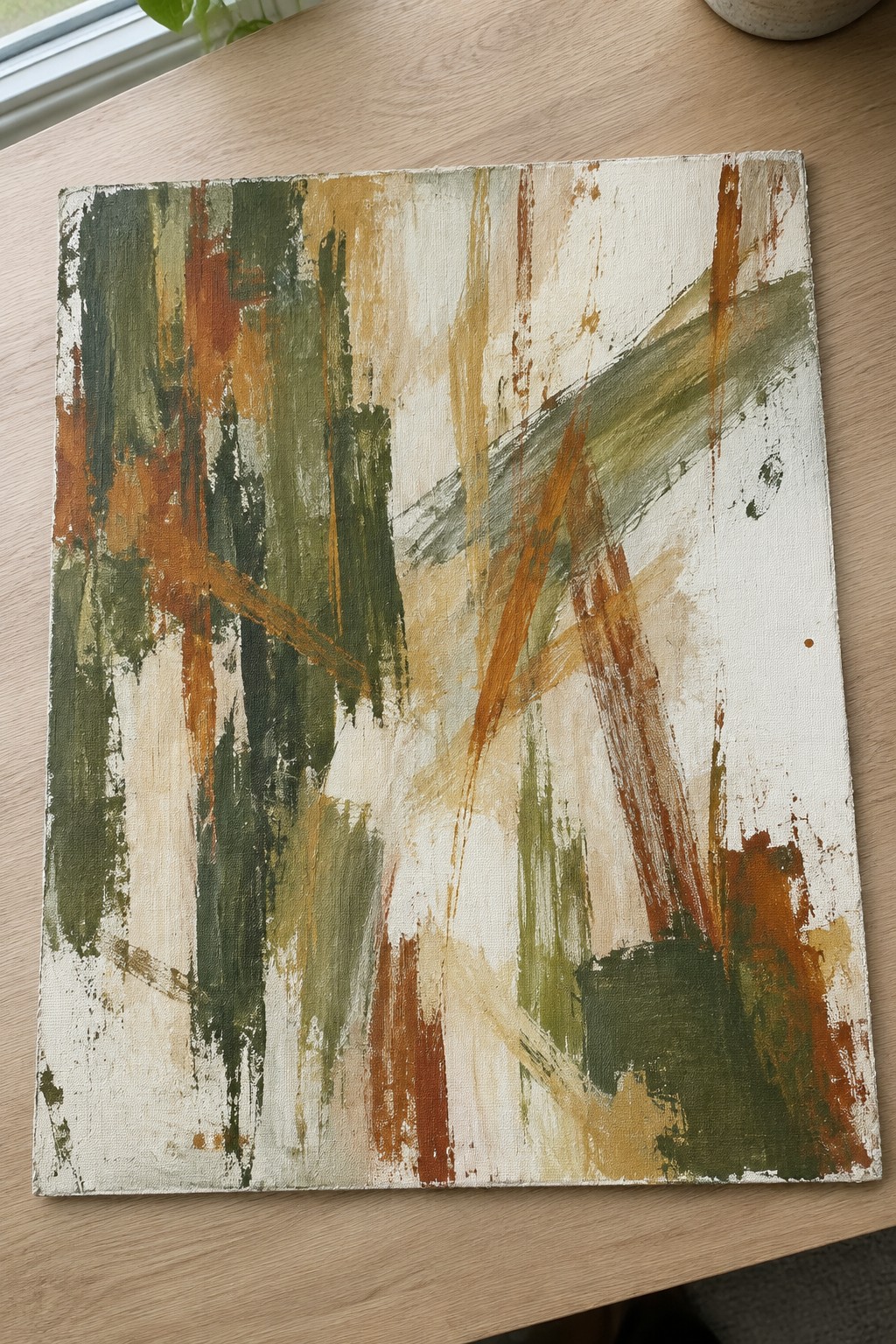 Abstract painting with green, orange, and brown brushstrokes on wooden table
