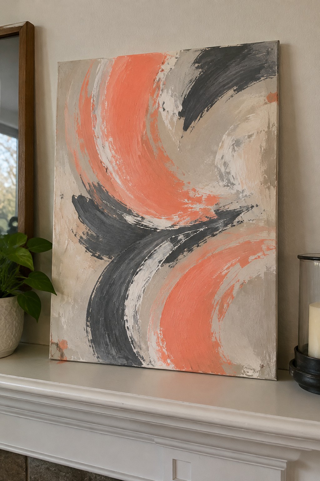 Abstract painting with coral, black, and gray swirls on white mantel beside plant and candle