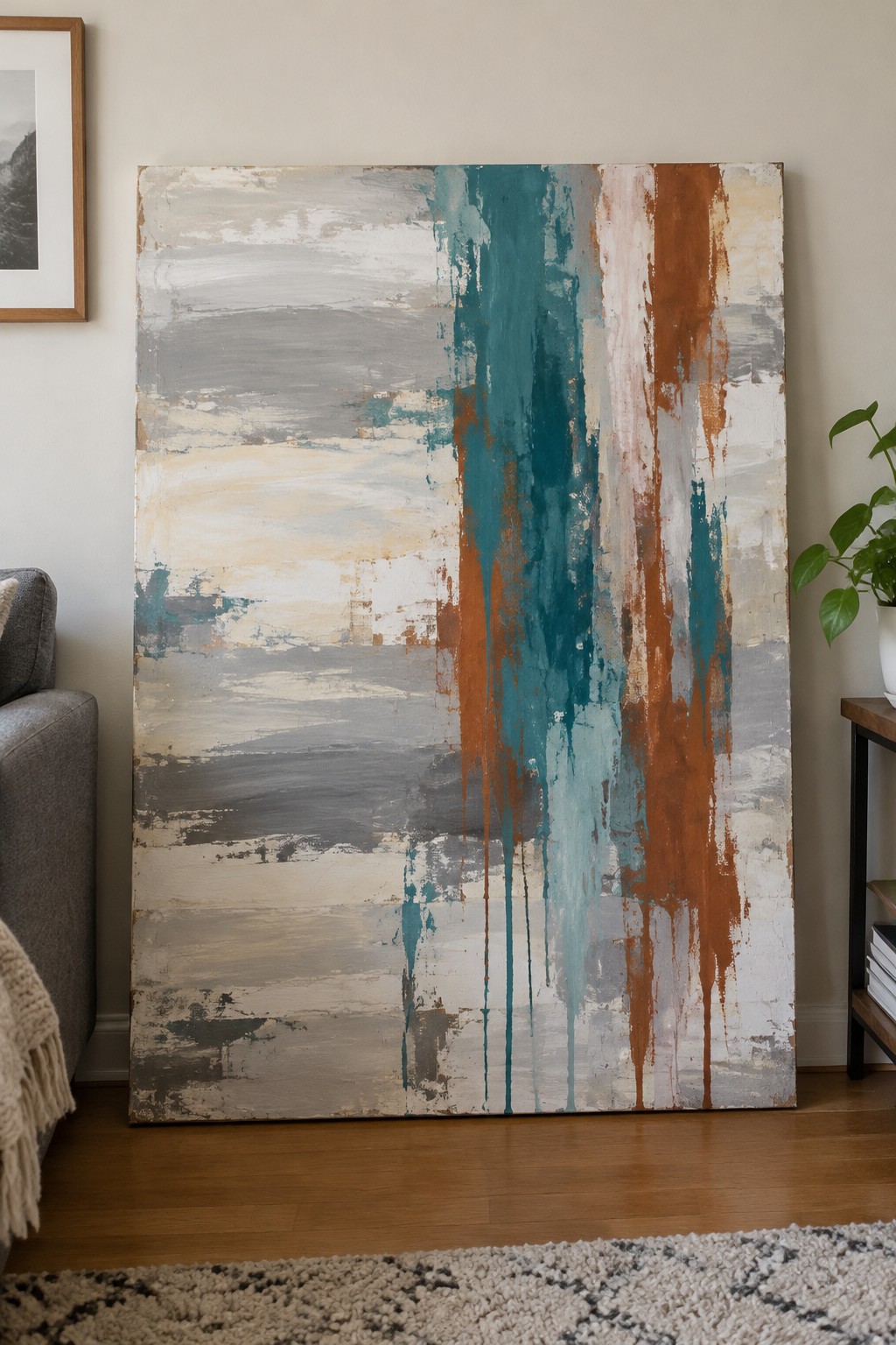 Large abstract painting with teal, rust, and gray drips leaning on wall