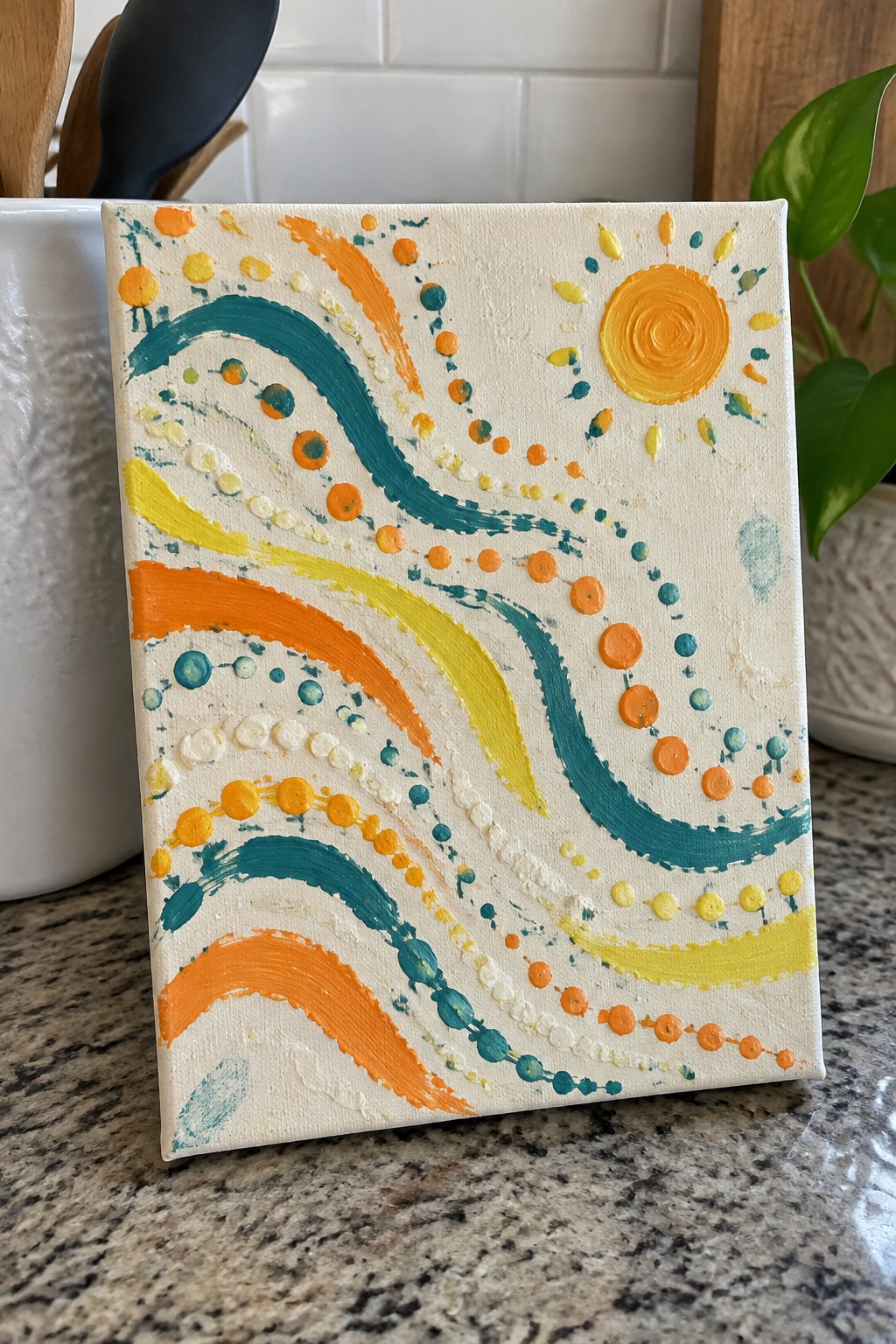Colorful abstract canvas with teal orange yellow swirls, dots, and sun on kitchen counter