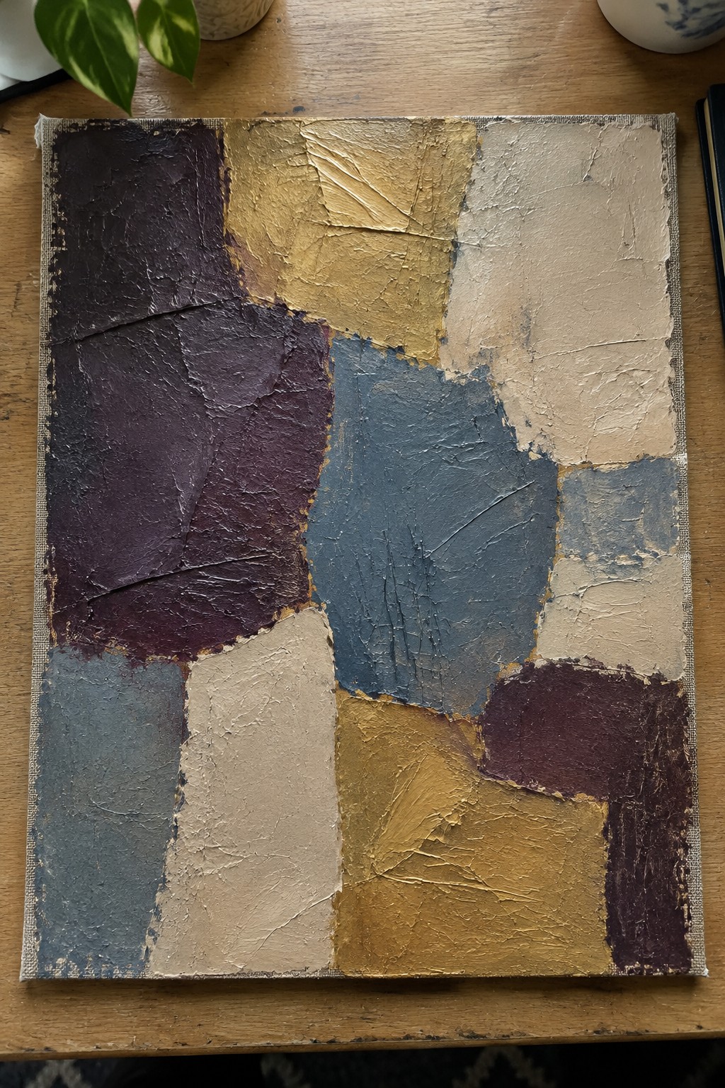 Abstract impasto painting in purple, gold, blue, and beige on wooden table