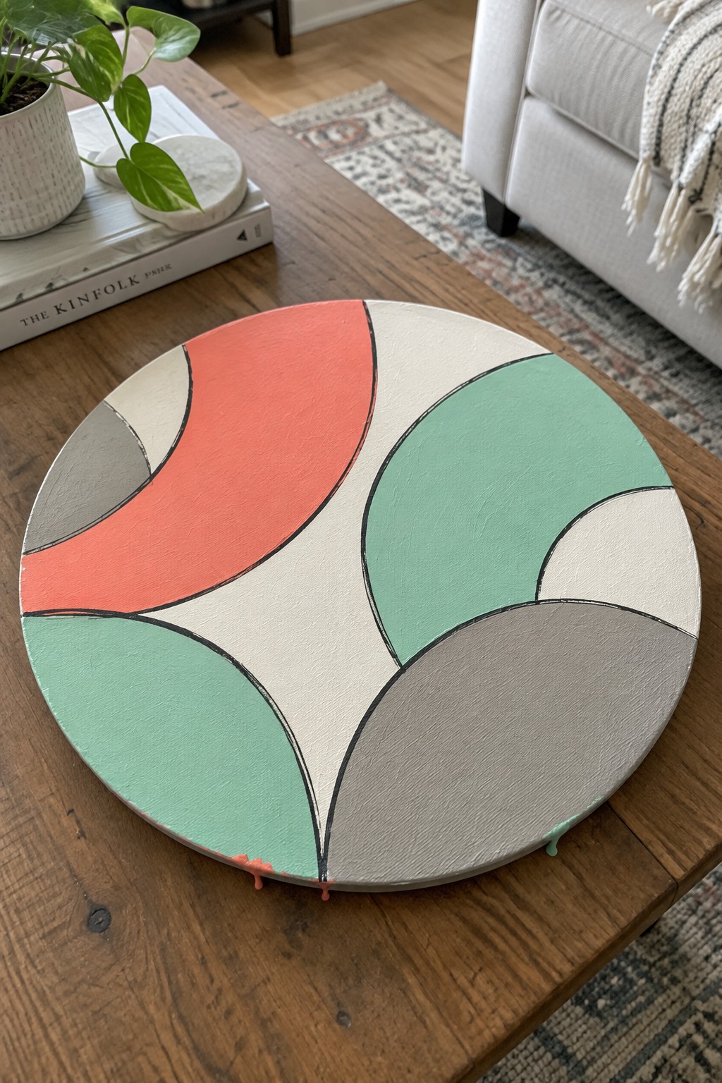 Abstract round canvas with curved coral, mint, gray, and cream shapes on wood table