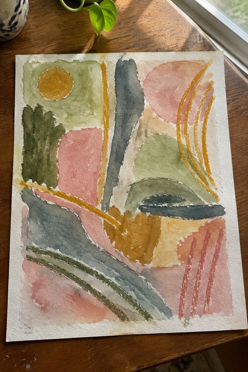 Abstract watercolor painting with colorful shapes on wooden table near green plant