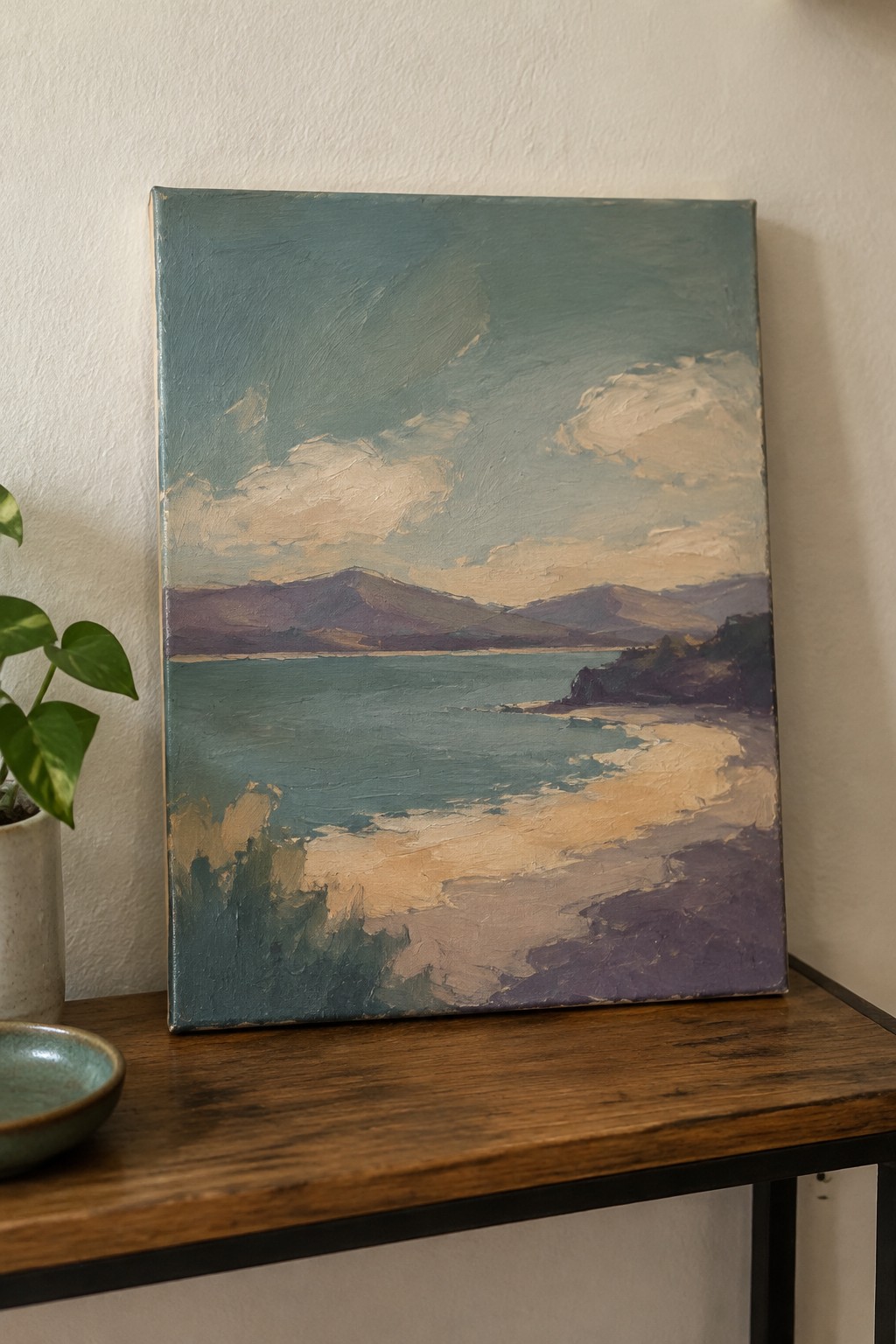 Impressionistic seascape painting on wooden table beside potted plant and ceramic bowl.