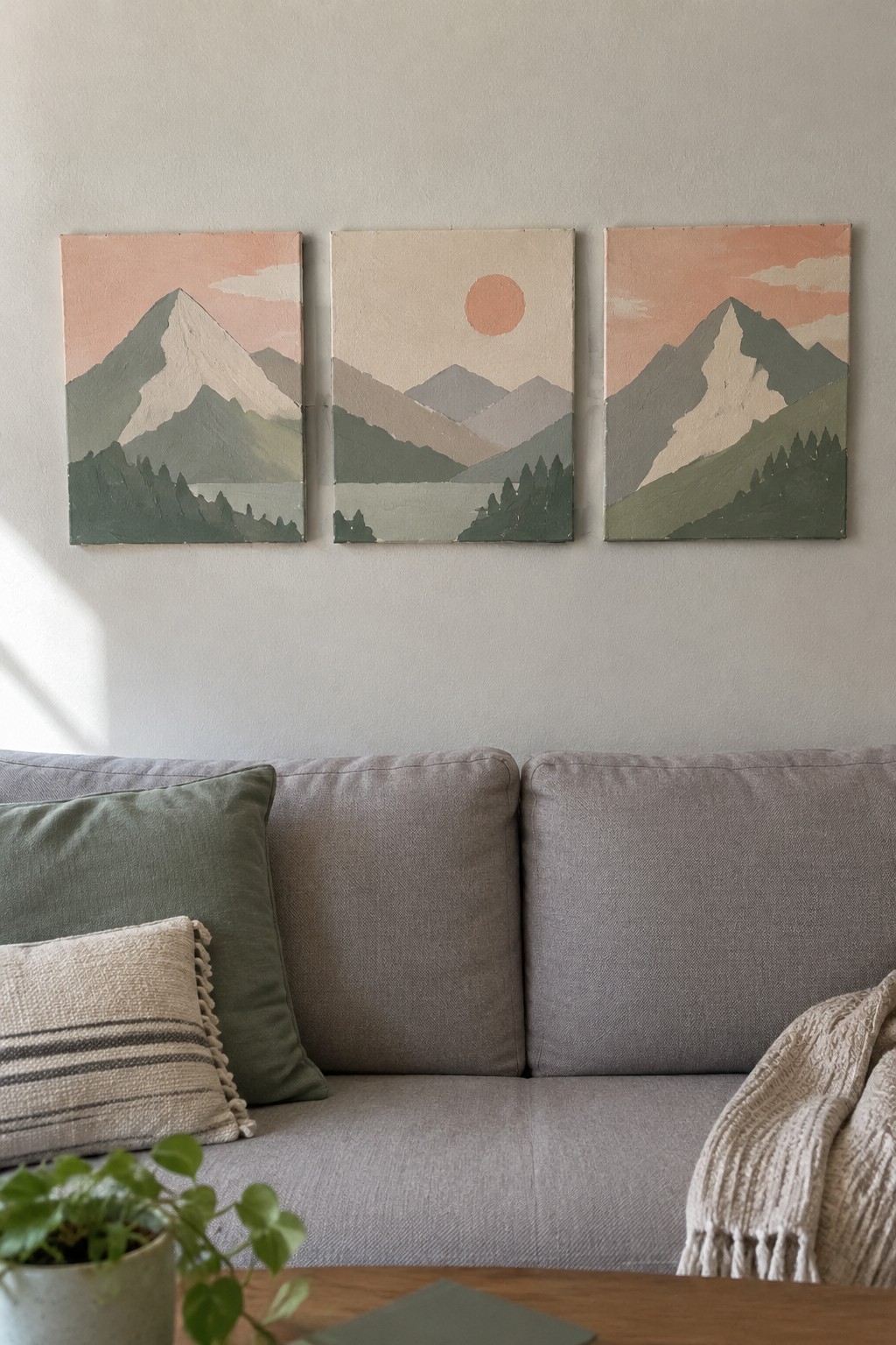 Three mountain landscape paintings above gray couch with green pillows and plant