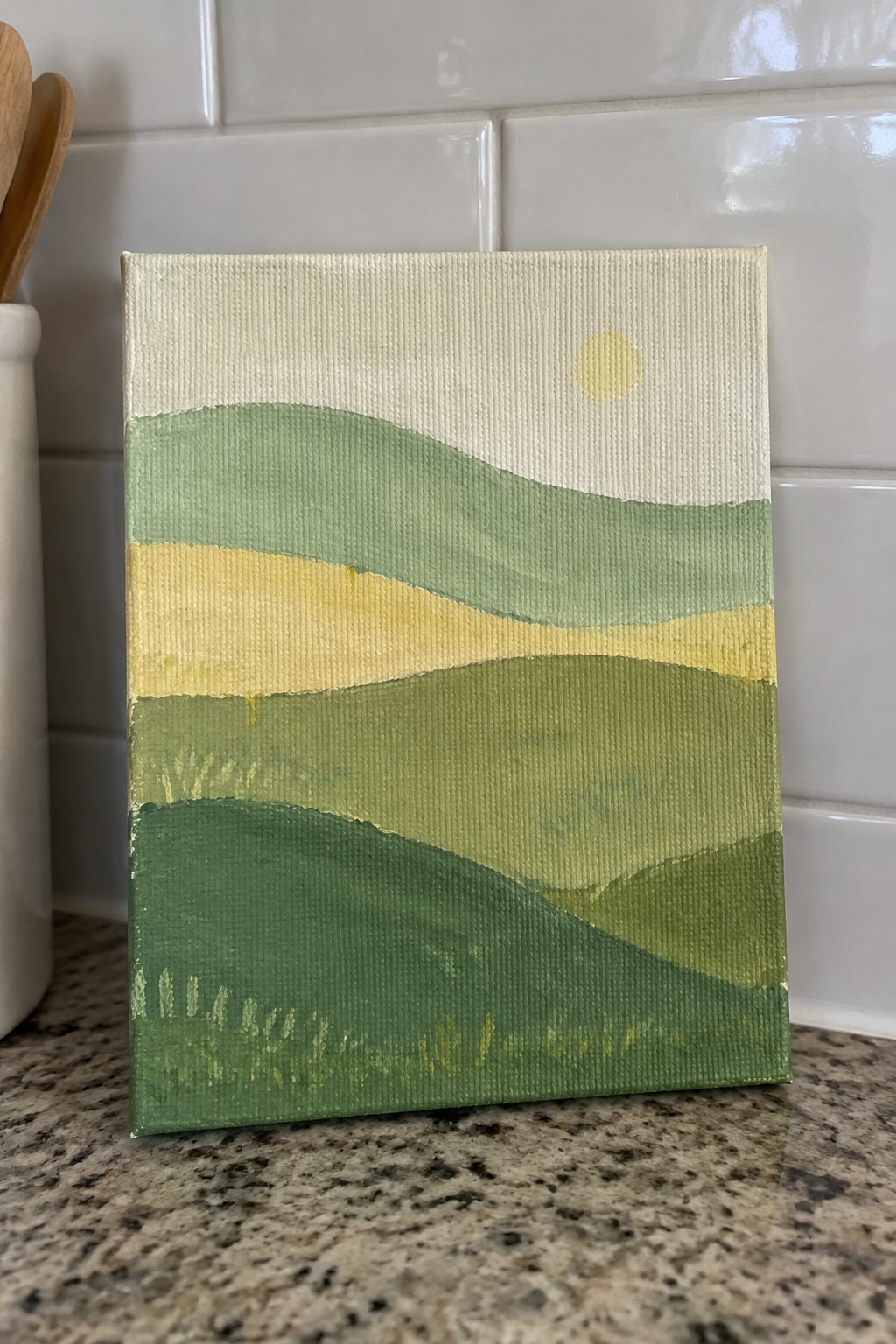Abstract landscape painting of rolling green hills with yellow sun on kitchen counter