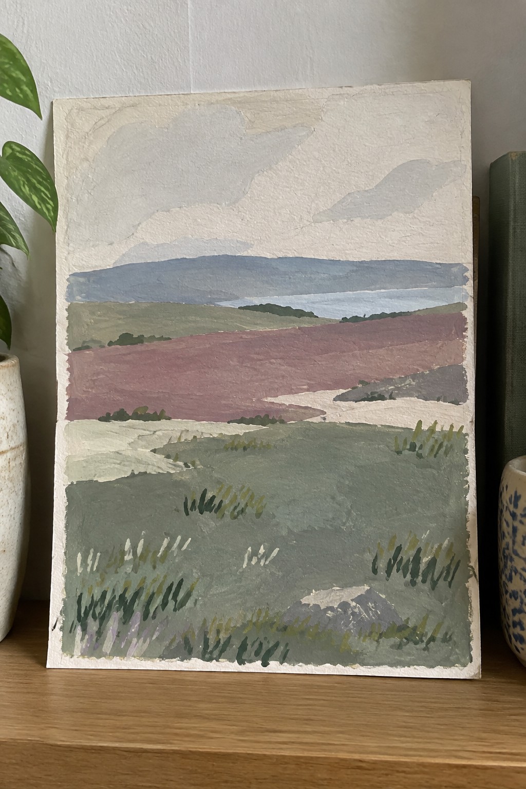Textured landscape painting of layered hills in green, purple and blue on wood shelf