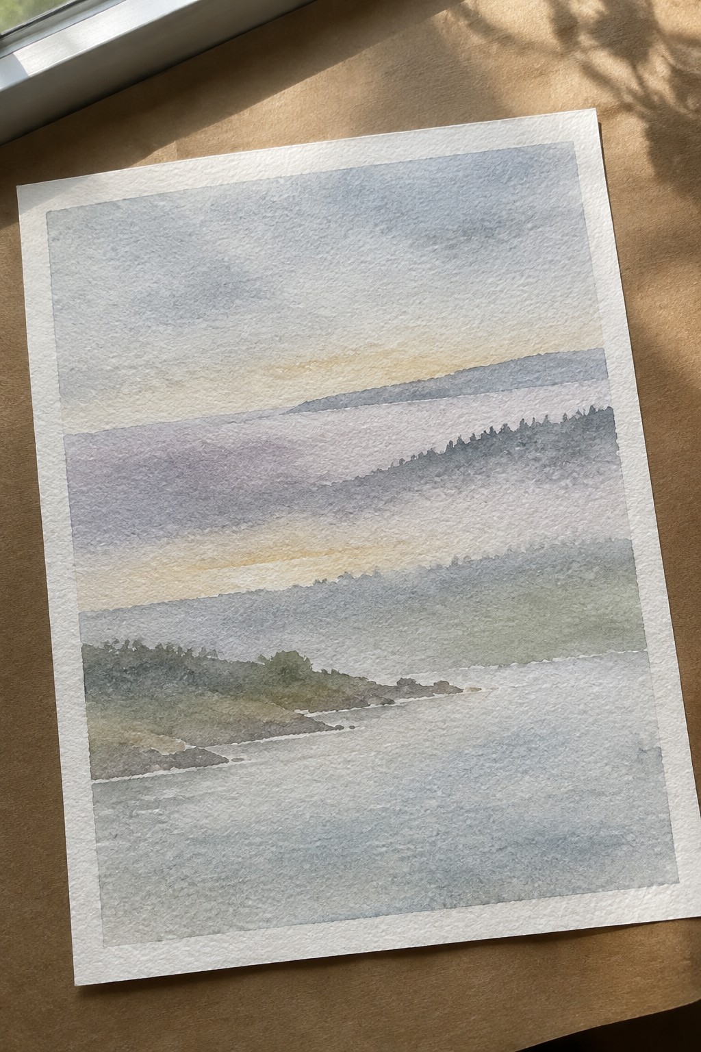 Watercolor of misty layered hills above a calm body of water at dawn.