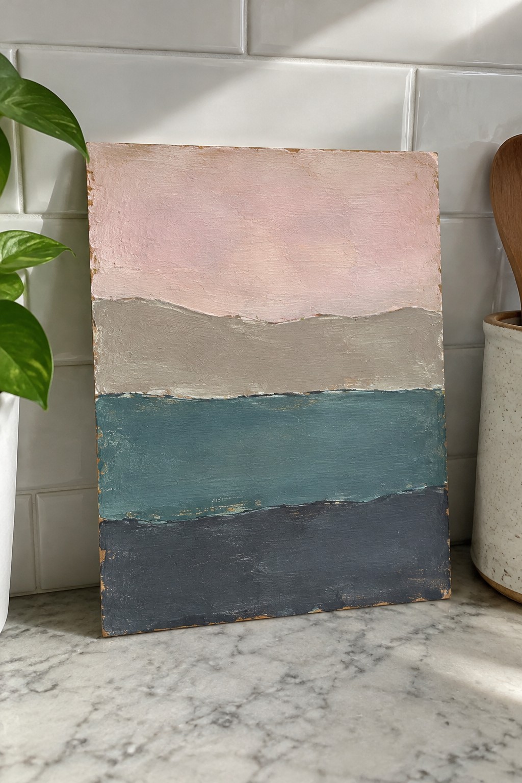 Abstract painting with pink, gray, teal, and dark gray layers on marble counter