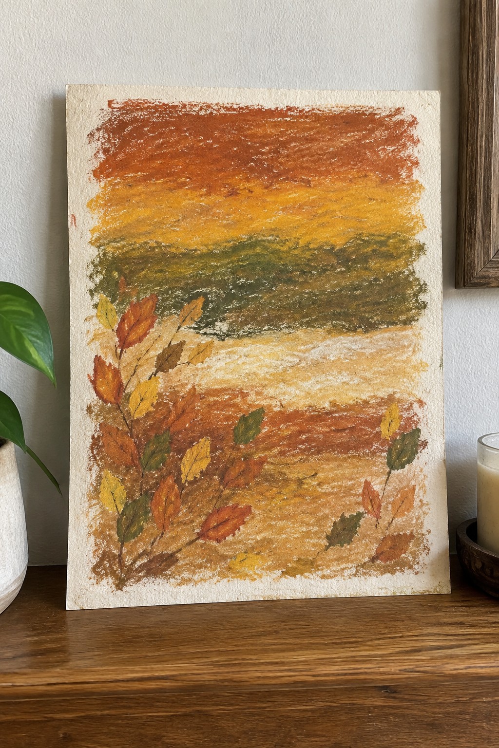 Autumn landscape pastel with orange-yellow sky, green band, brown path, and fall leaves.
