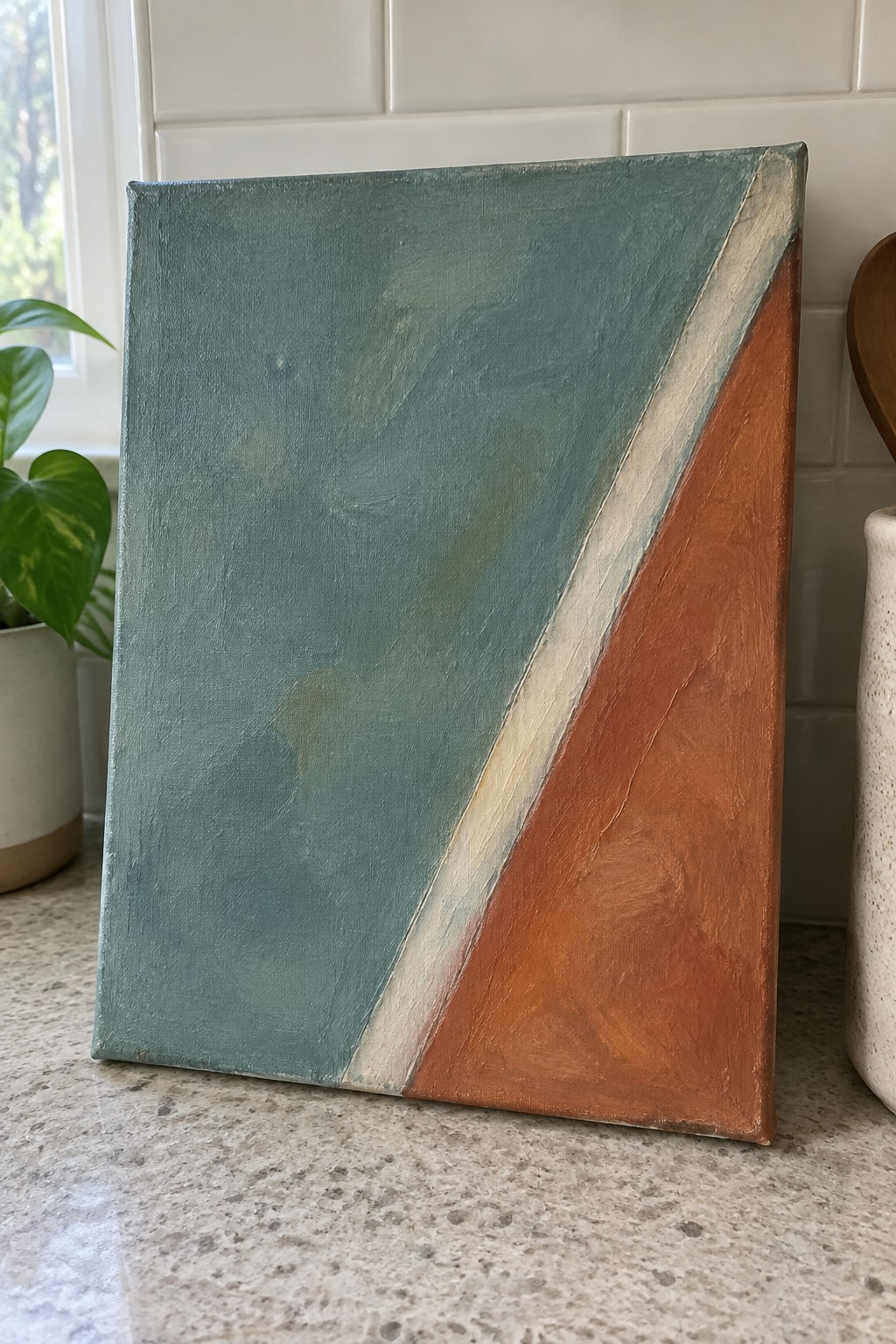 Abstract canvas painting with teal, cream, and terracotta diagonal sections on countertop