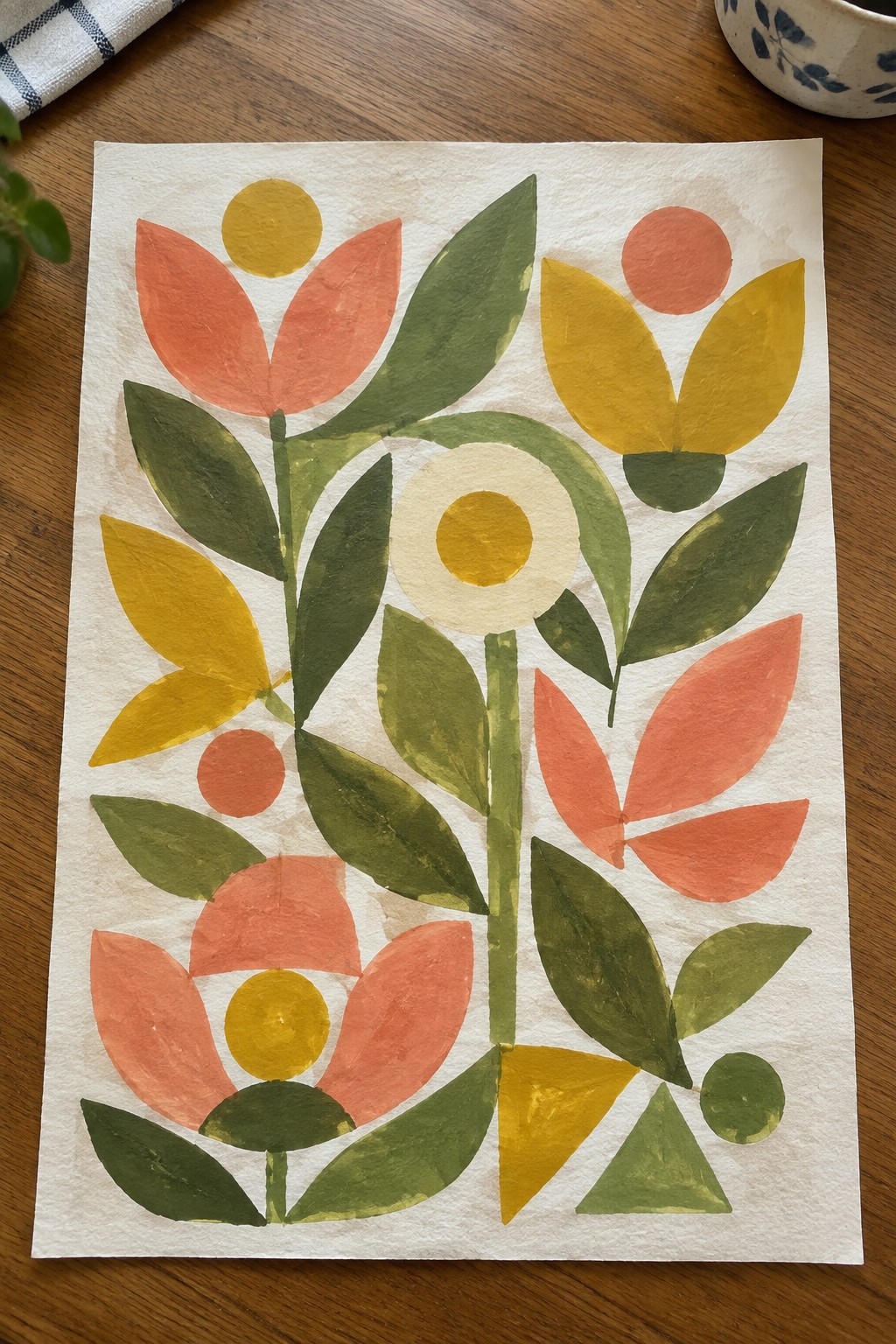 Vibrant cut-paper floral collage with coral, yellow, and green leaves on white paper over wood