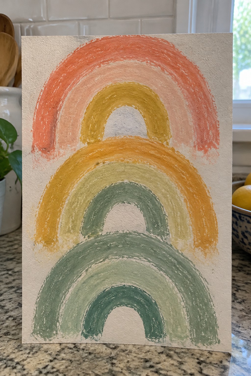 Watercolor rainbow with orange, yellow, and green arches on textured white paper