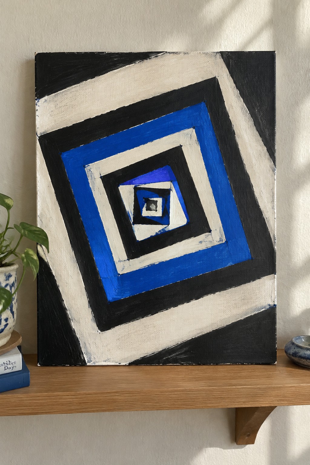 Abstract painting of concentric blue black white squares on shelf with potted plant