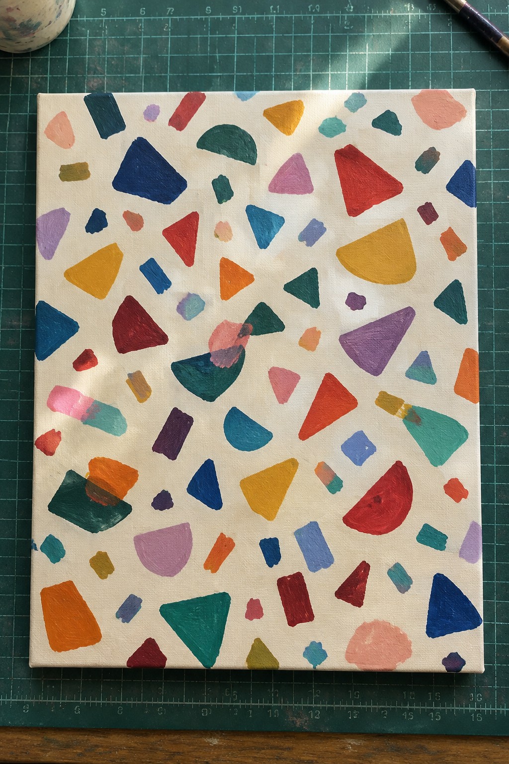 Abstract canvas with colorful geometric shapes on white background atop green cutting mat