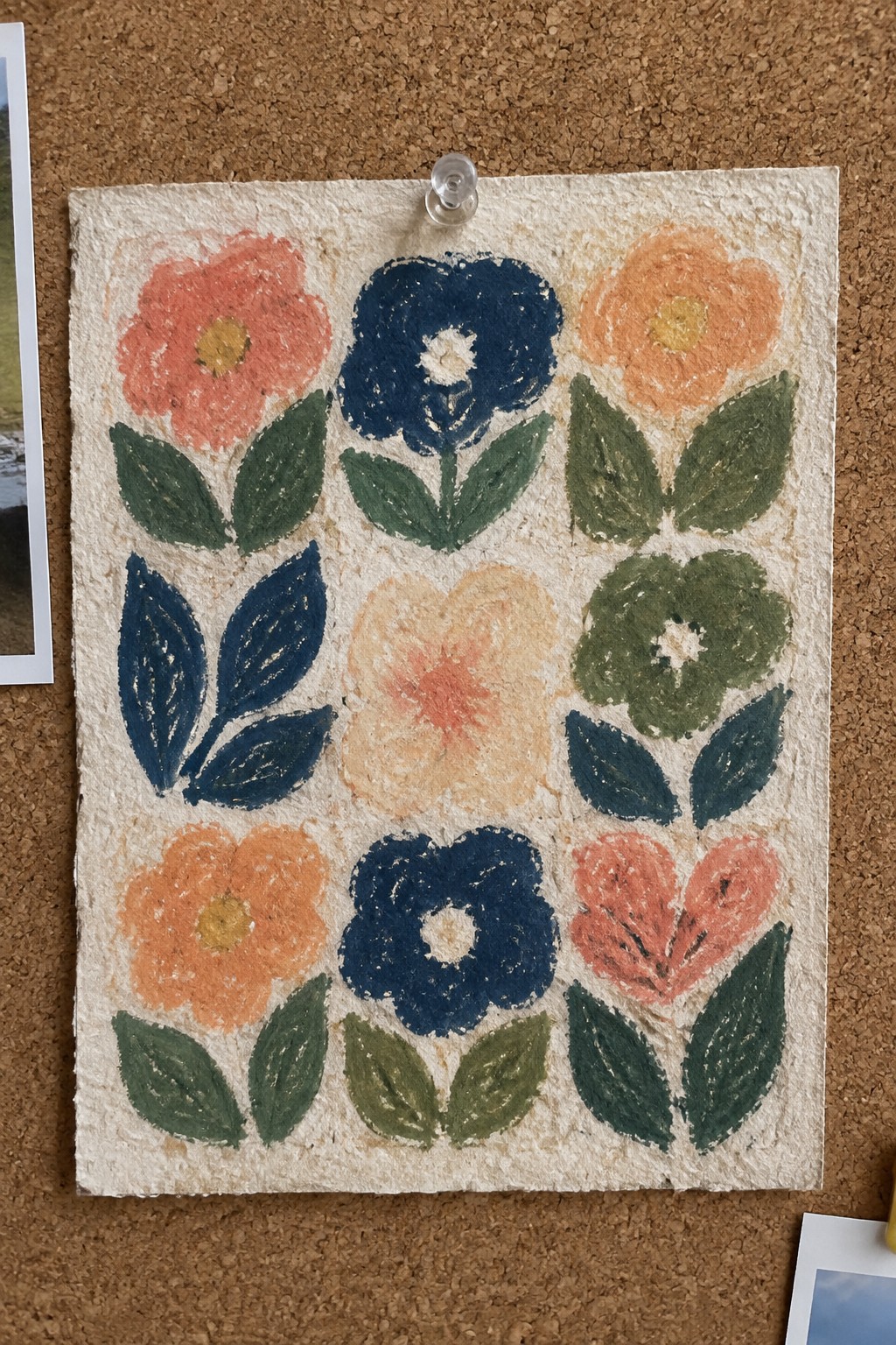 Eight stylized flowers in coral, navy blue, peach, and green with leaves arranged on textured paper pinned to corkboard.