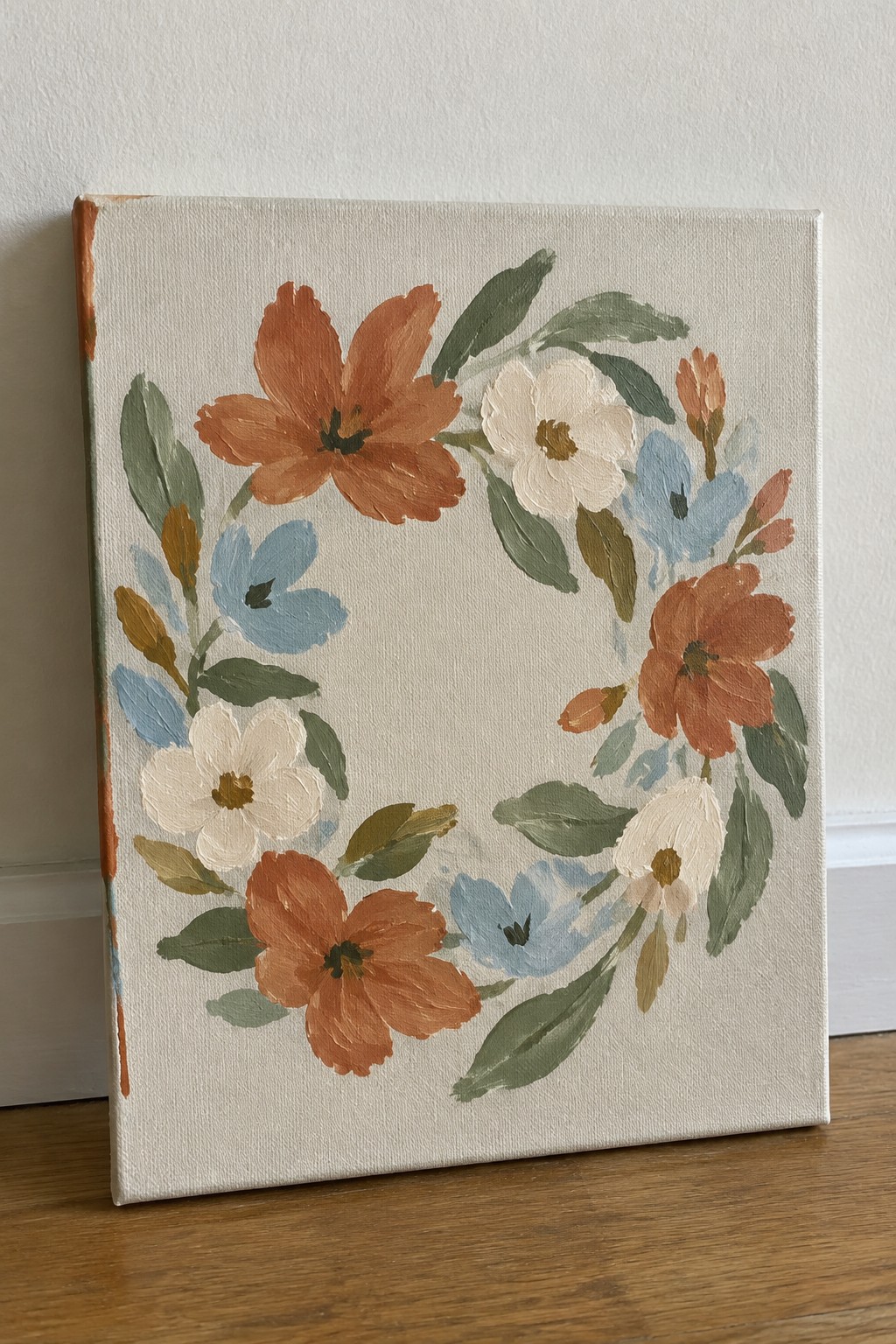 Canvas painting of circular floral wreath with orange, white, blue flowers and green leaves