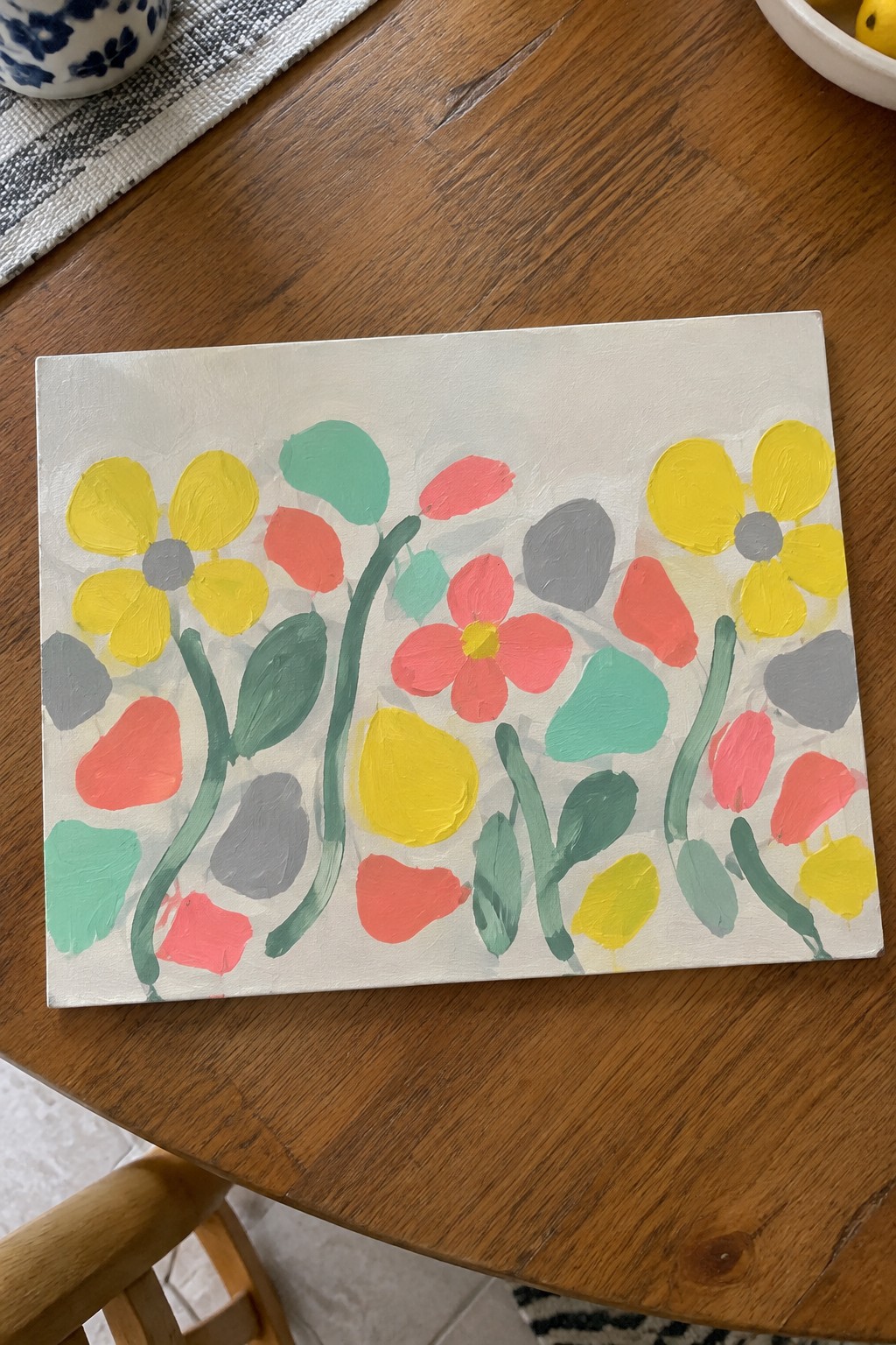 Colorful abstract floral painting with yellow, pink flowers, green stems, and teal leaves on canvas