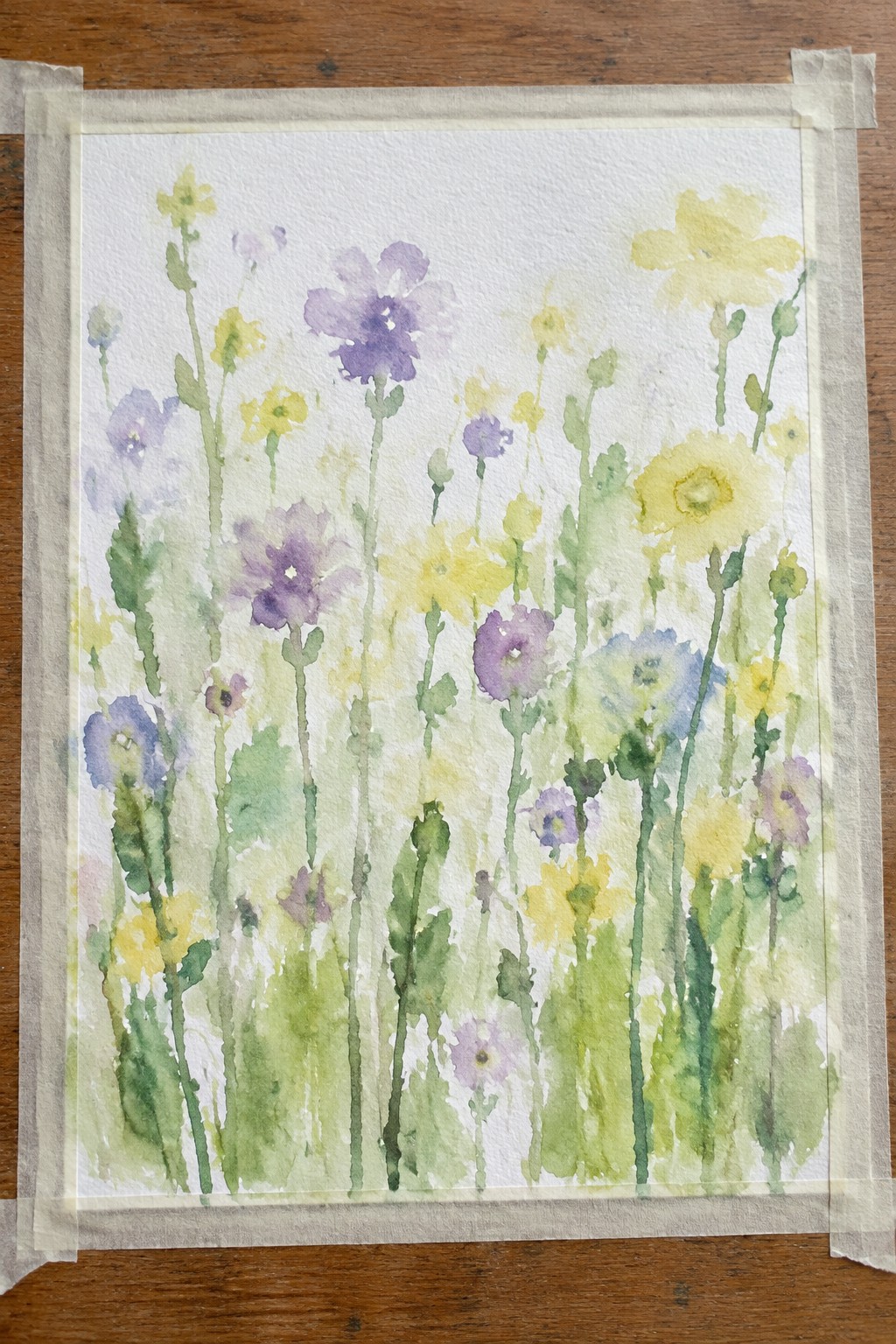 Watercolor wildflowers in purple, yellow, and blue taped to wooden surface